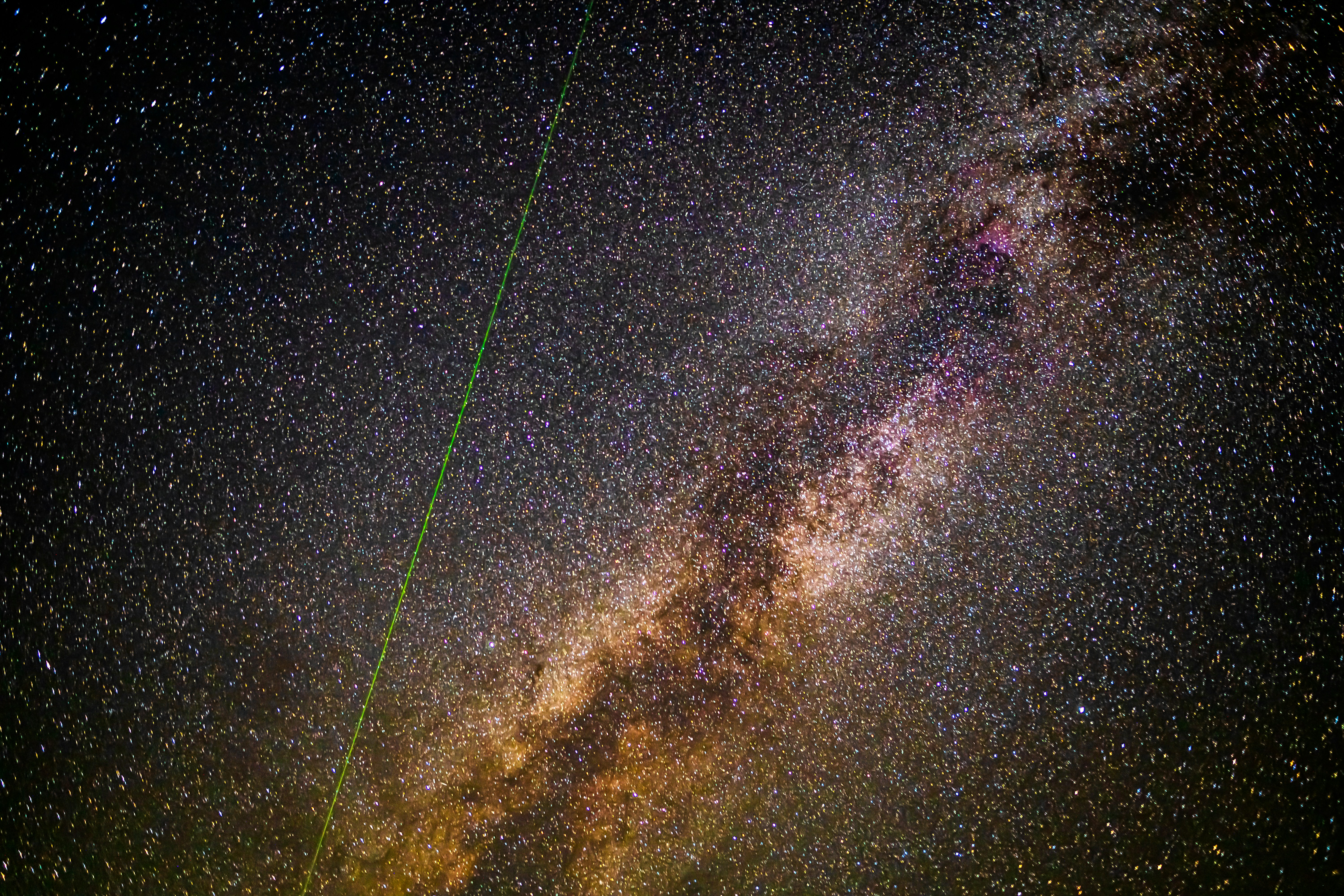 A bright green laser beam cutting across the dense Milky Way galaxy