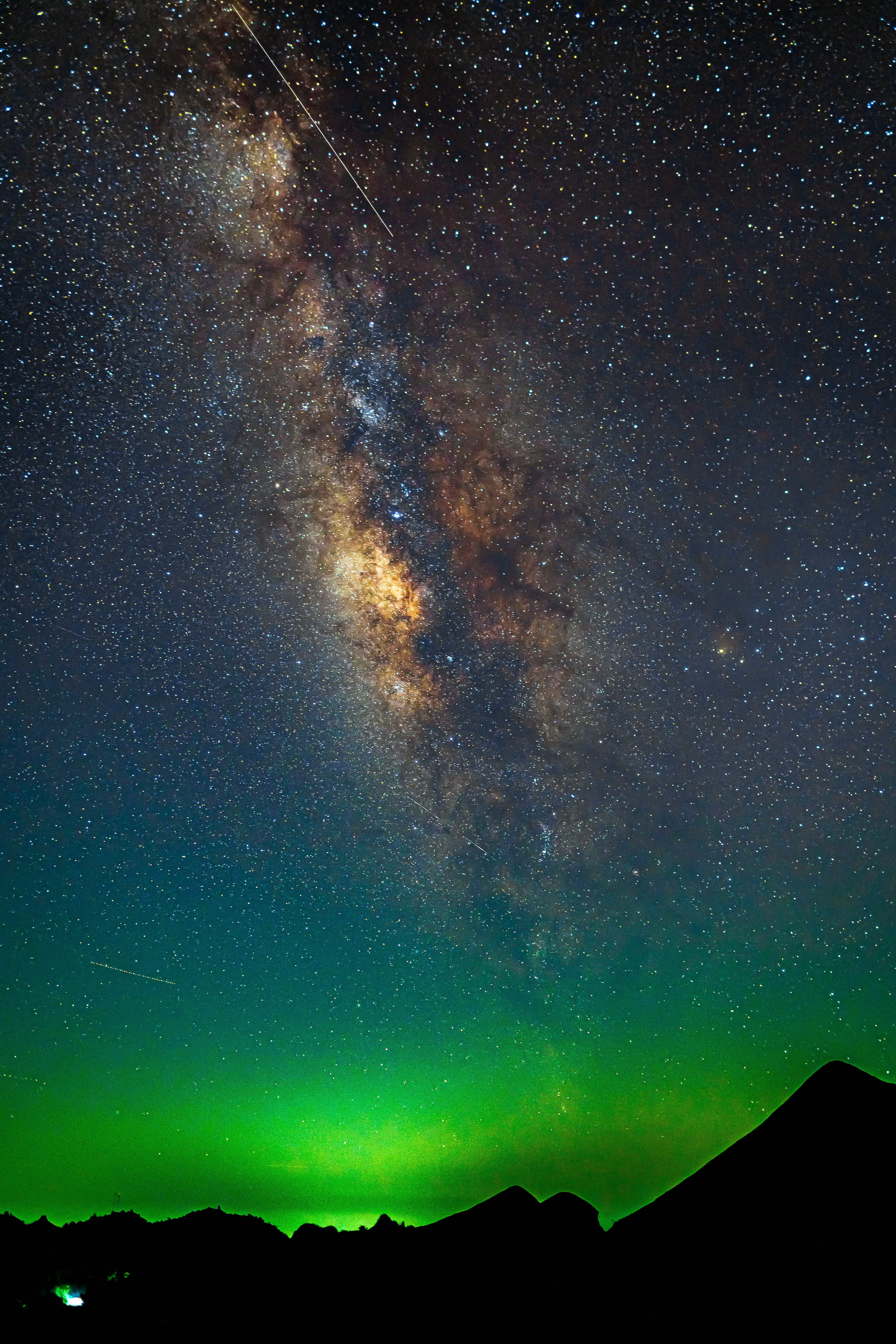 The Milky Way galaxy glowing above a dark mountain silhouette and green airglow