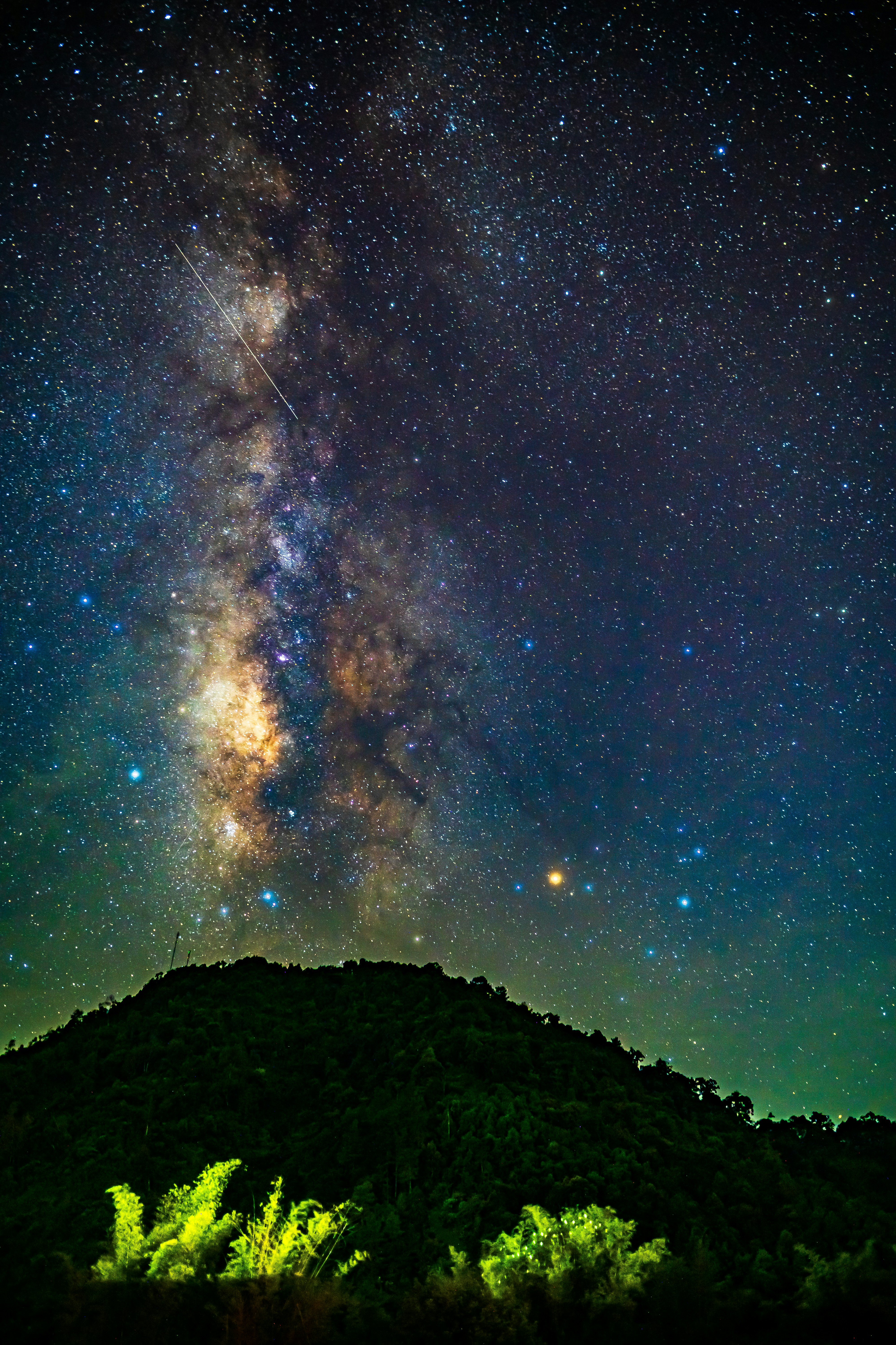 The Milky Way galaxy stretching across a starry night sky above a dark hill