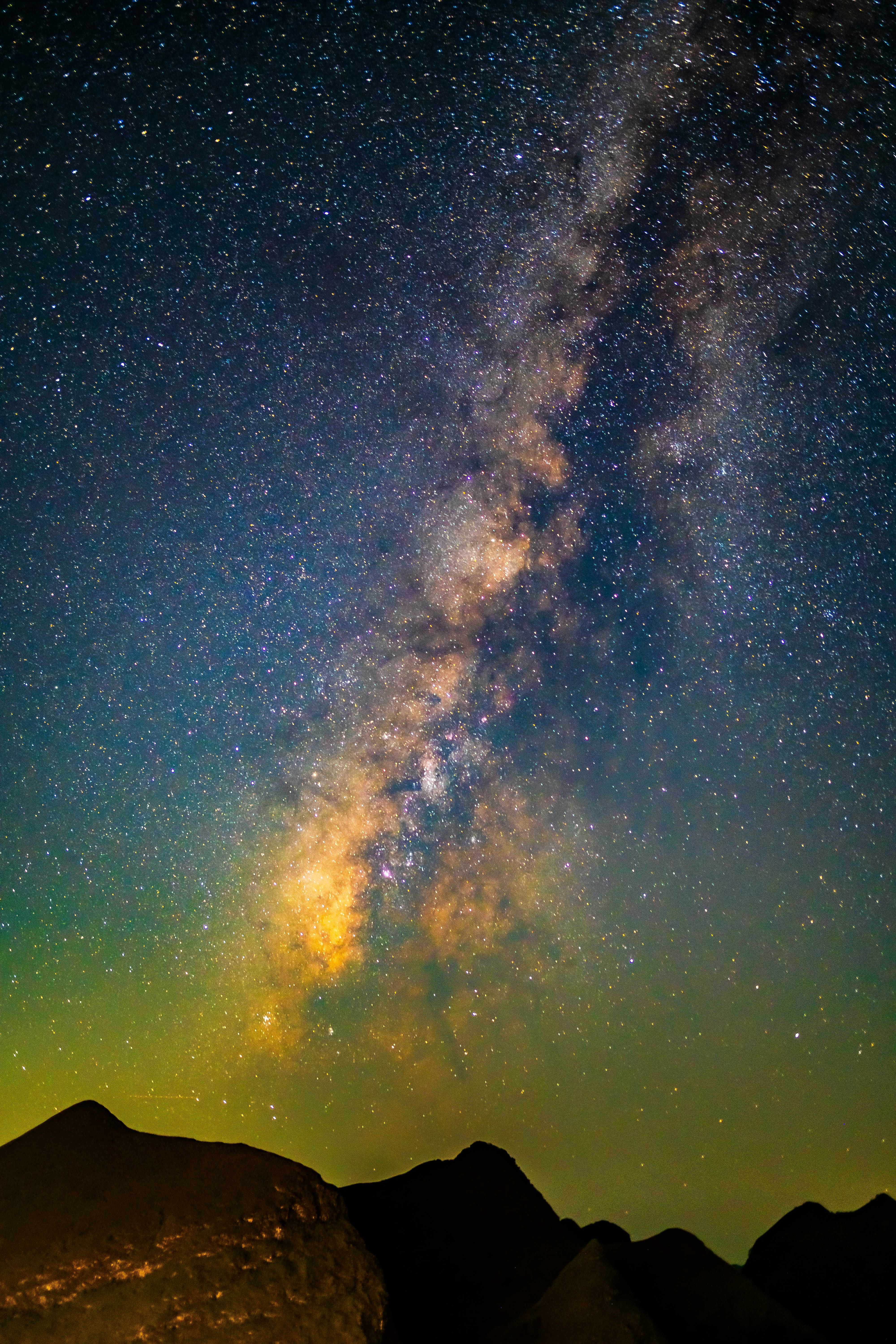 The Milky Way galaxy glowing above dark mountain silhouettes against a starry night sky
