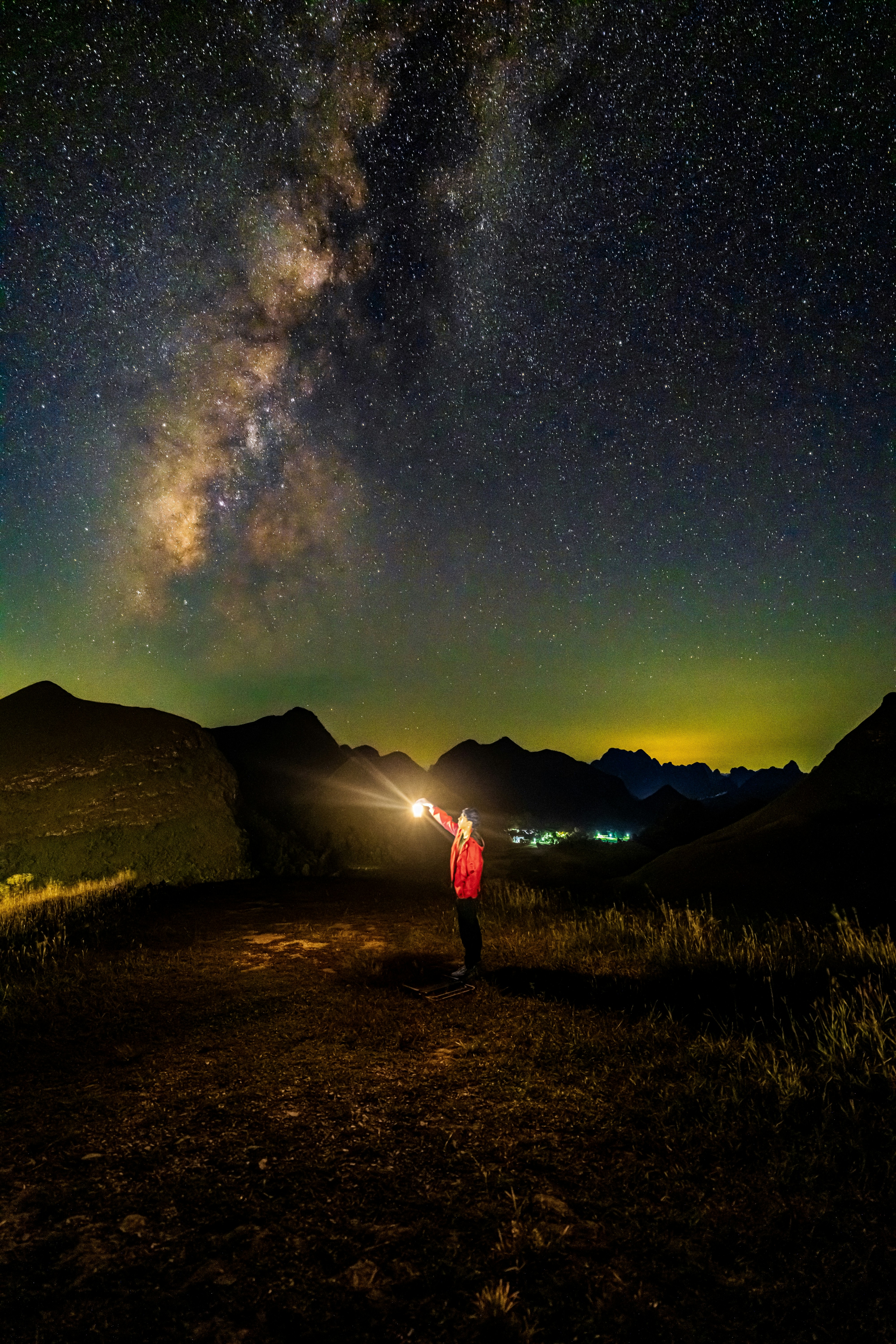 A person in a red jacket holding a lantern under a starry night sky