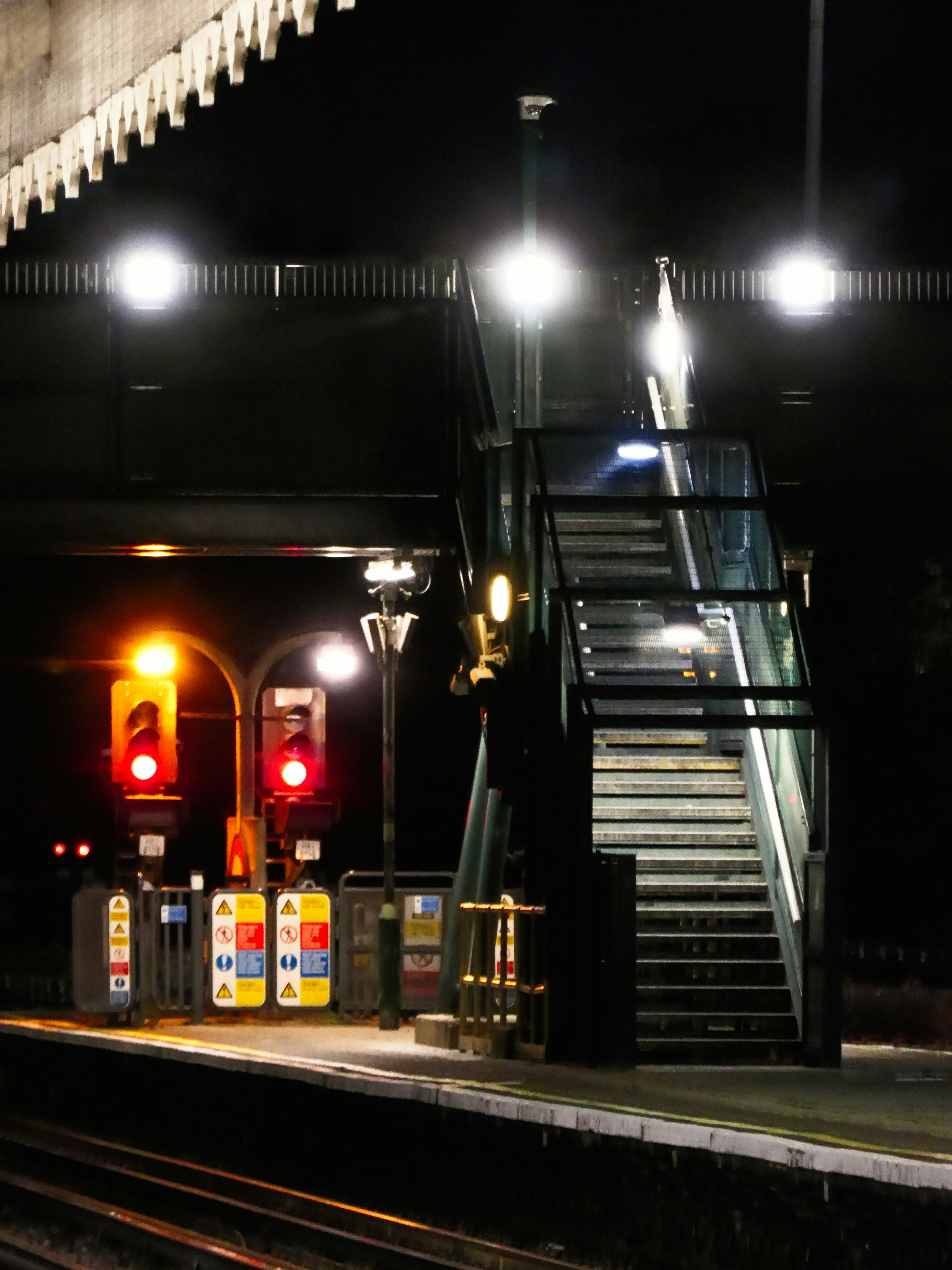 A railway platform at night with illuminated red signals and a metal staircase