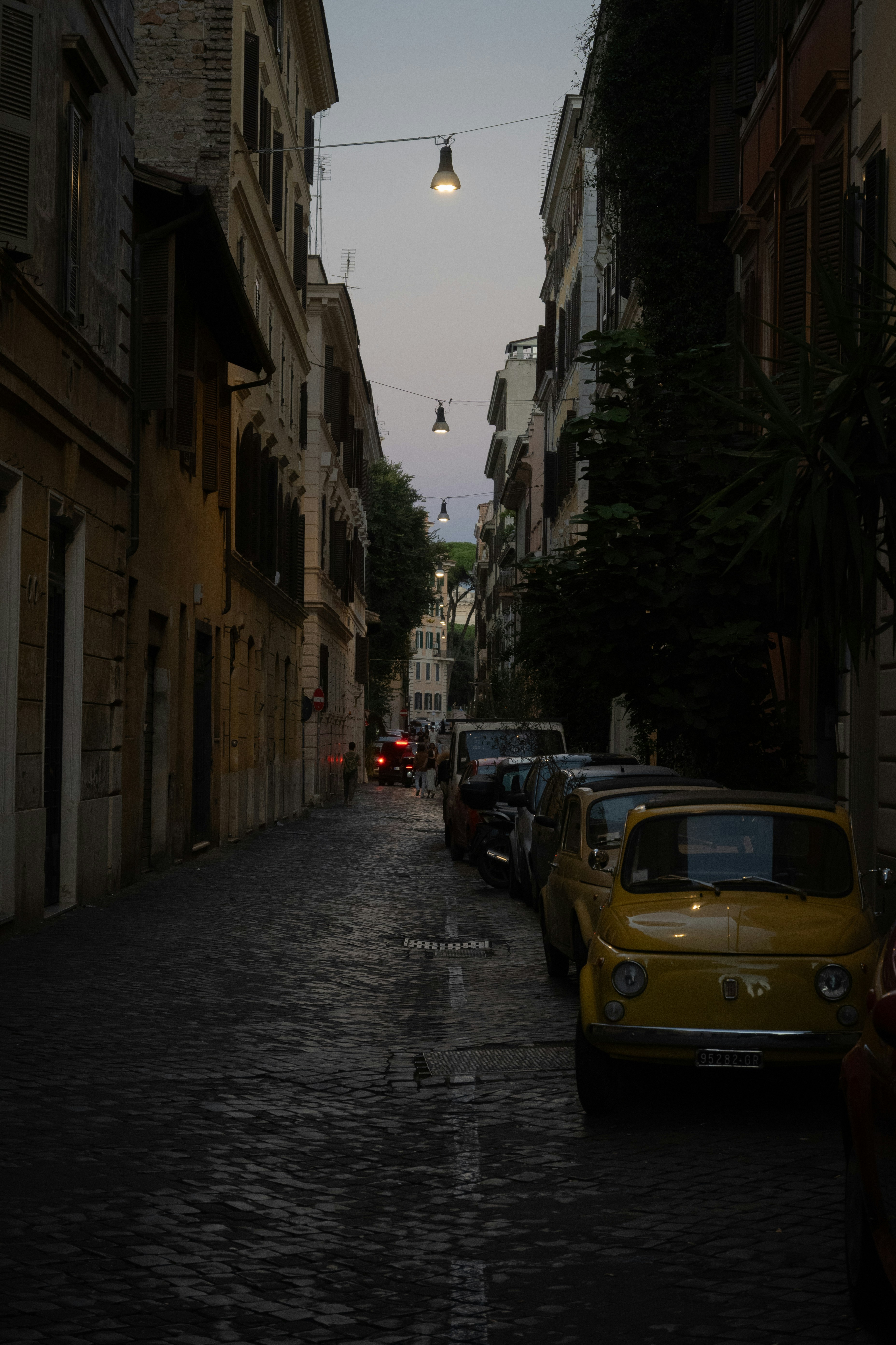 A yellow Fiat 500 parked on a narrow cobblestone street in Rome