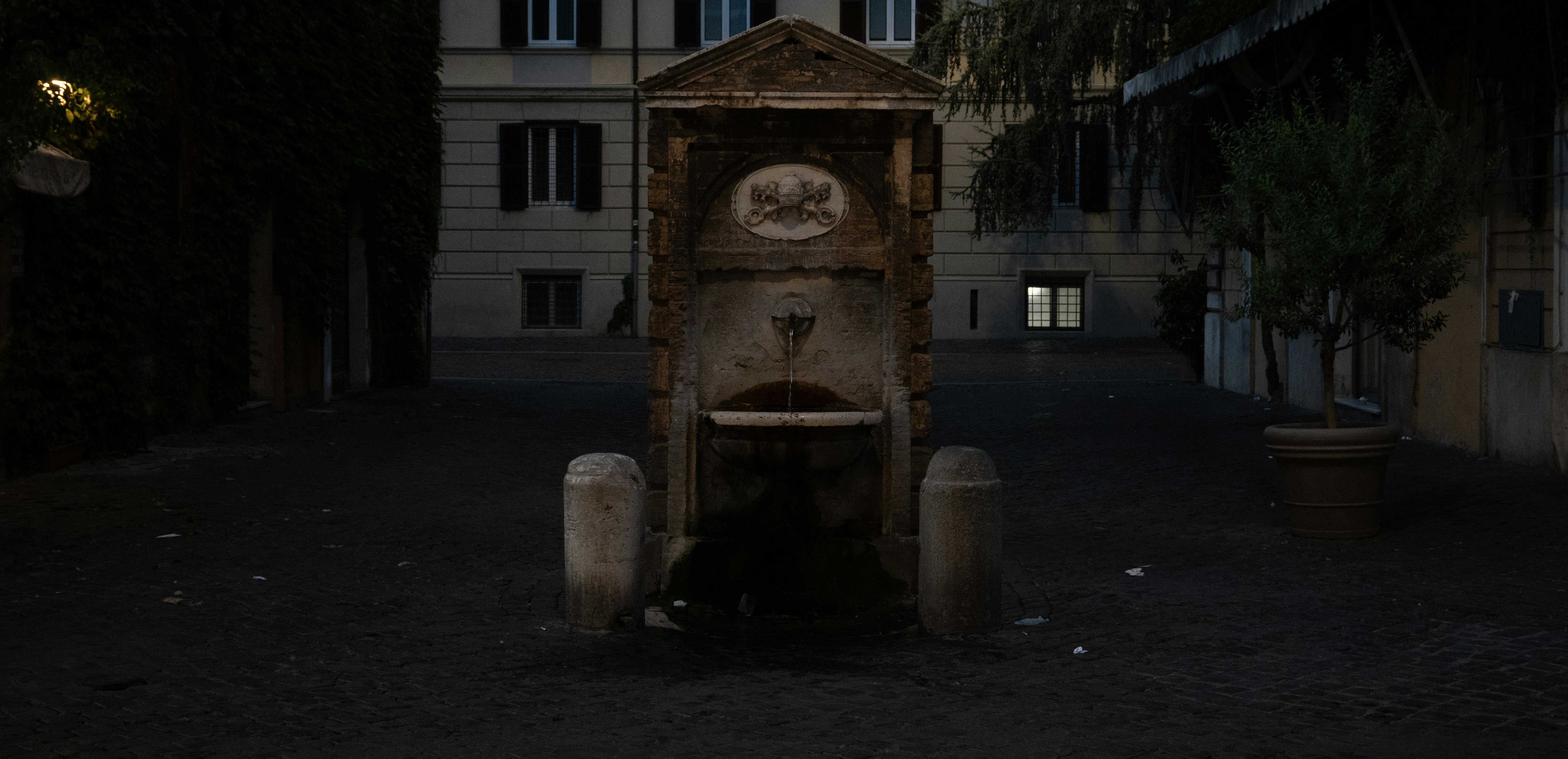 A stone fountain with a small basin in a dim city square