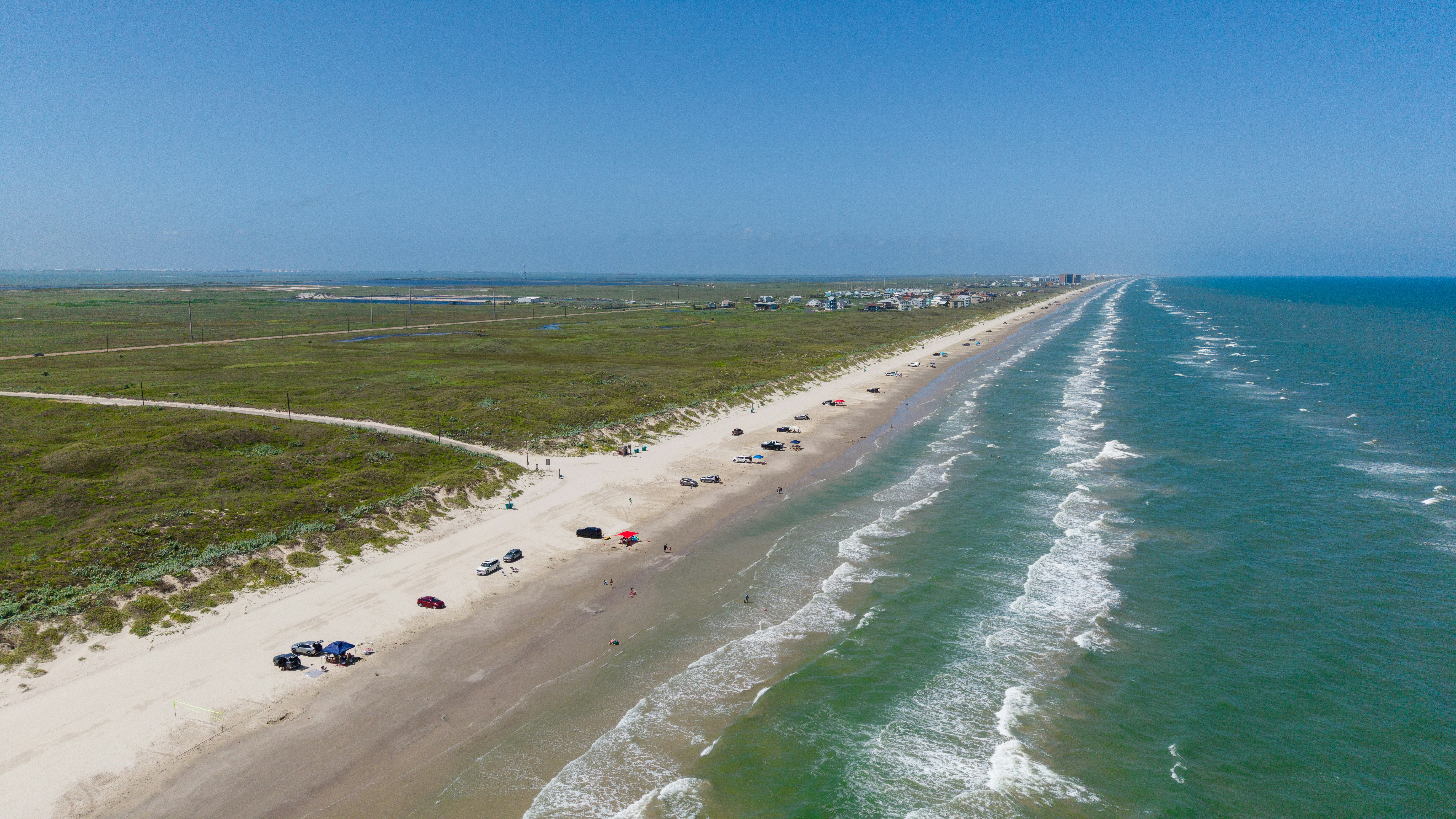 An aerial view of a long sandy beach with parked cars and ocean waves