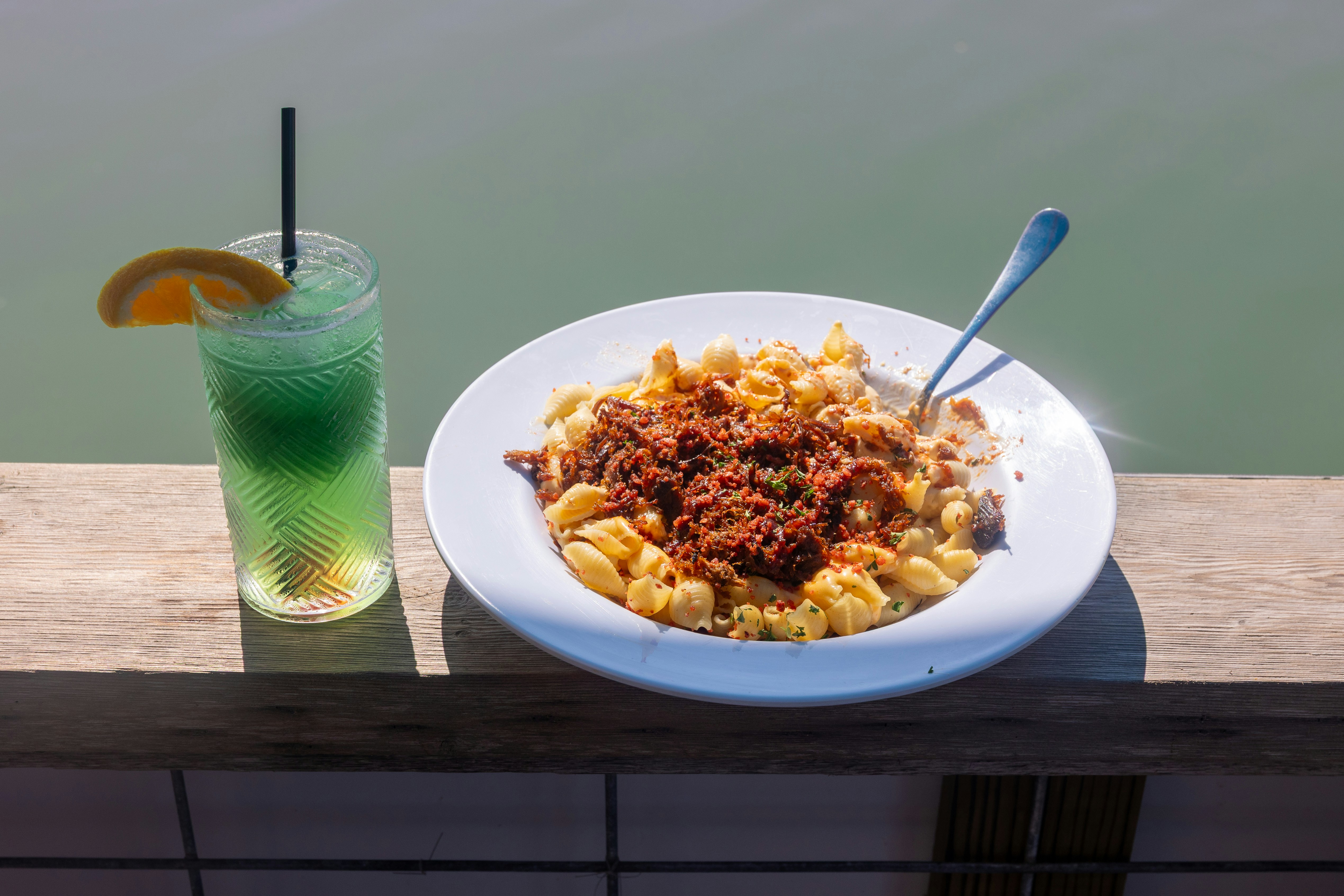 A plate of shell pasta with meat and a green cocktail on a wooden ledge