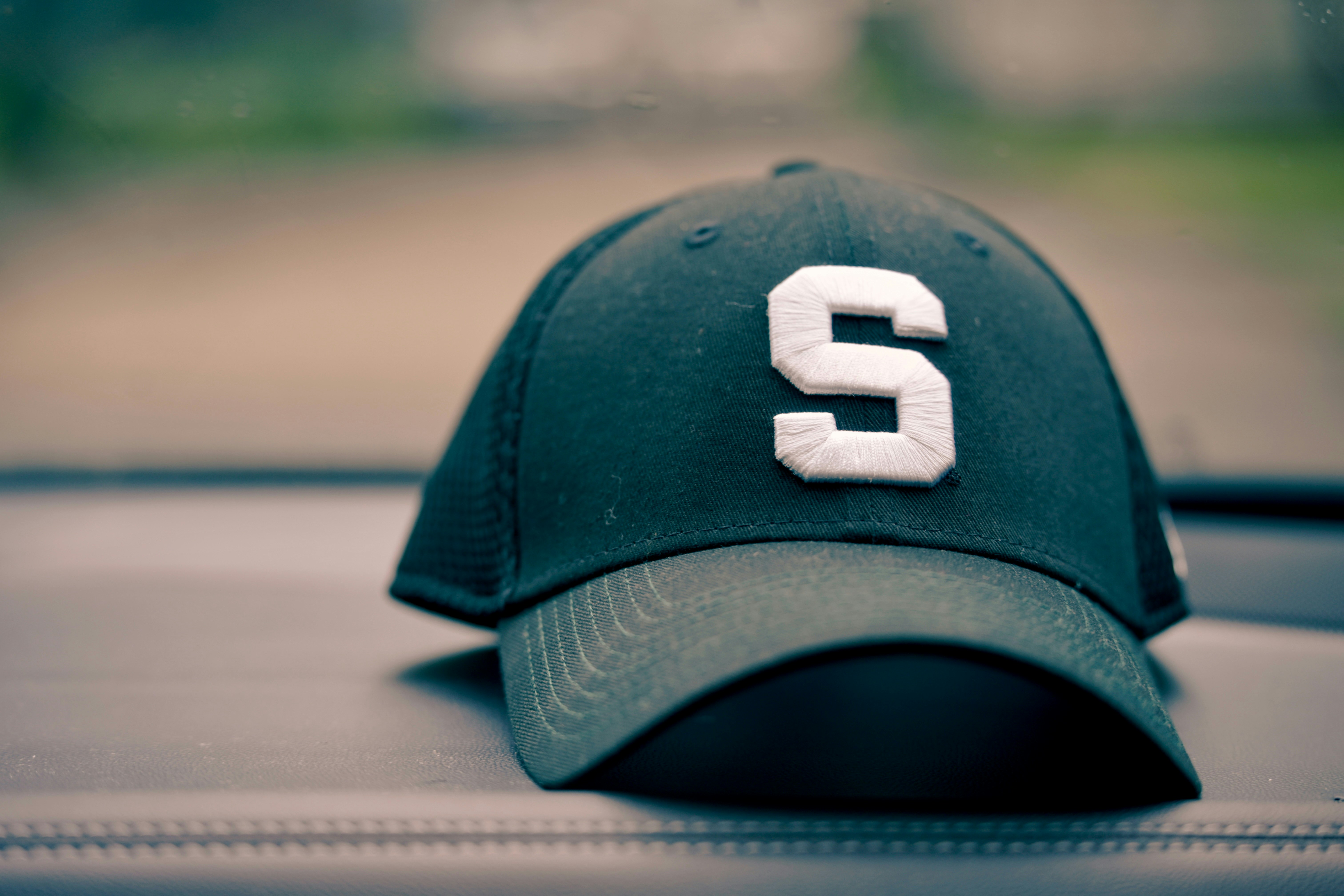 A dark green baseball cap with a white letter S on the dashboard