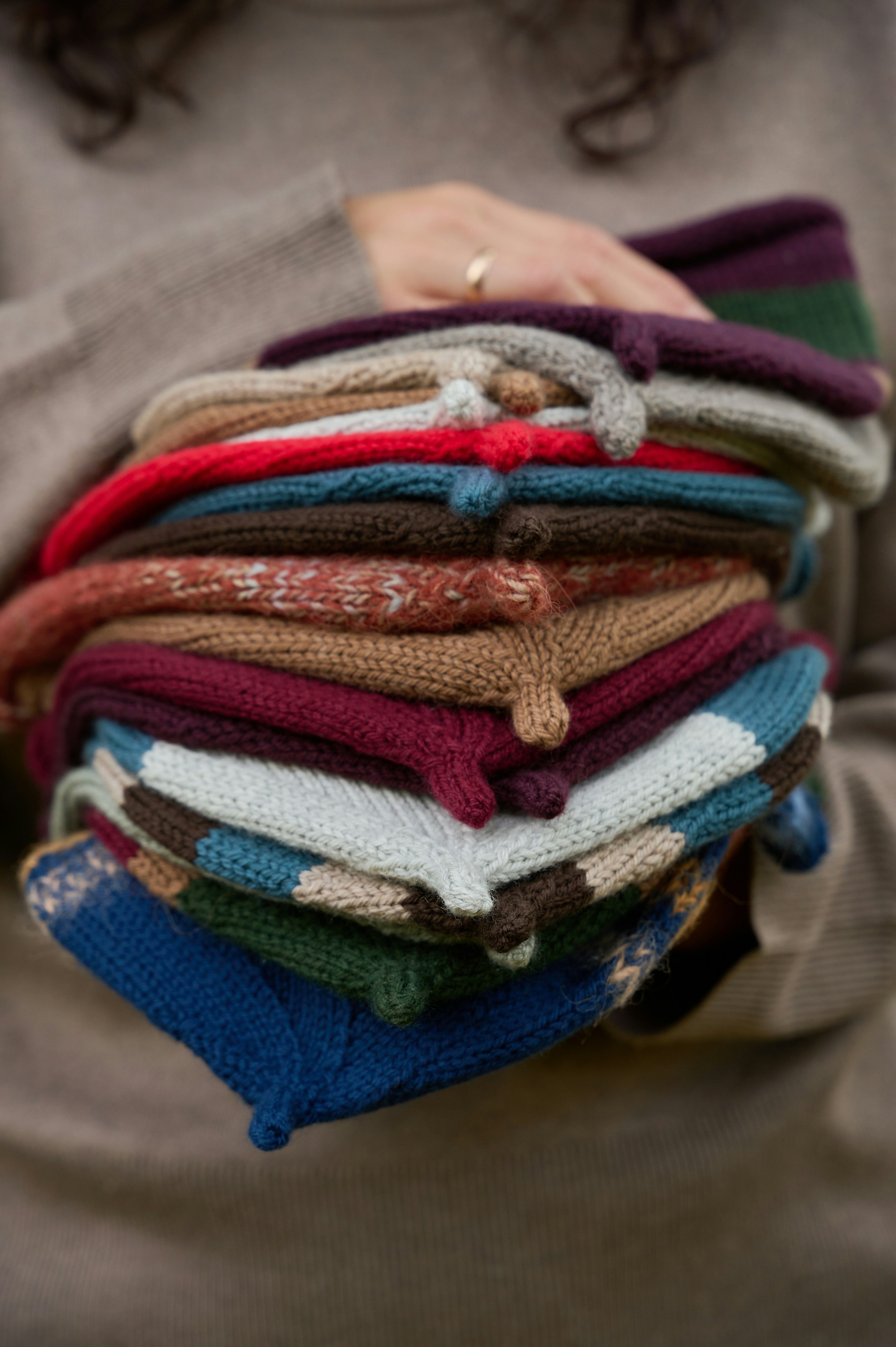 A person holding a stack of colorful folded knit hats in their arms