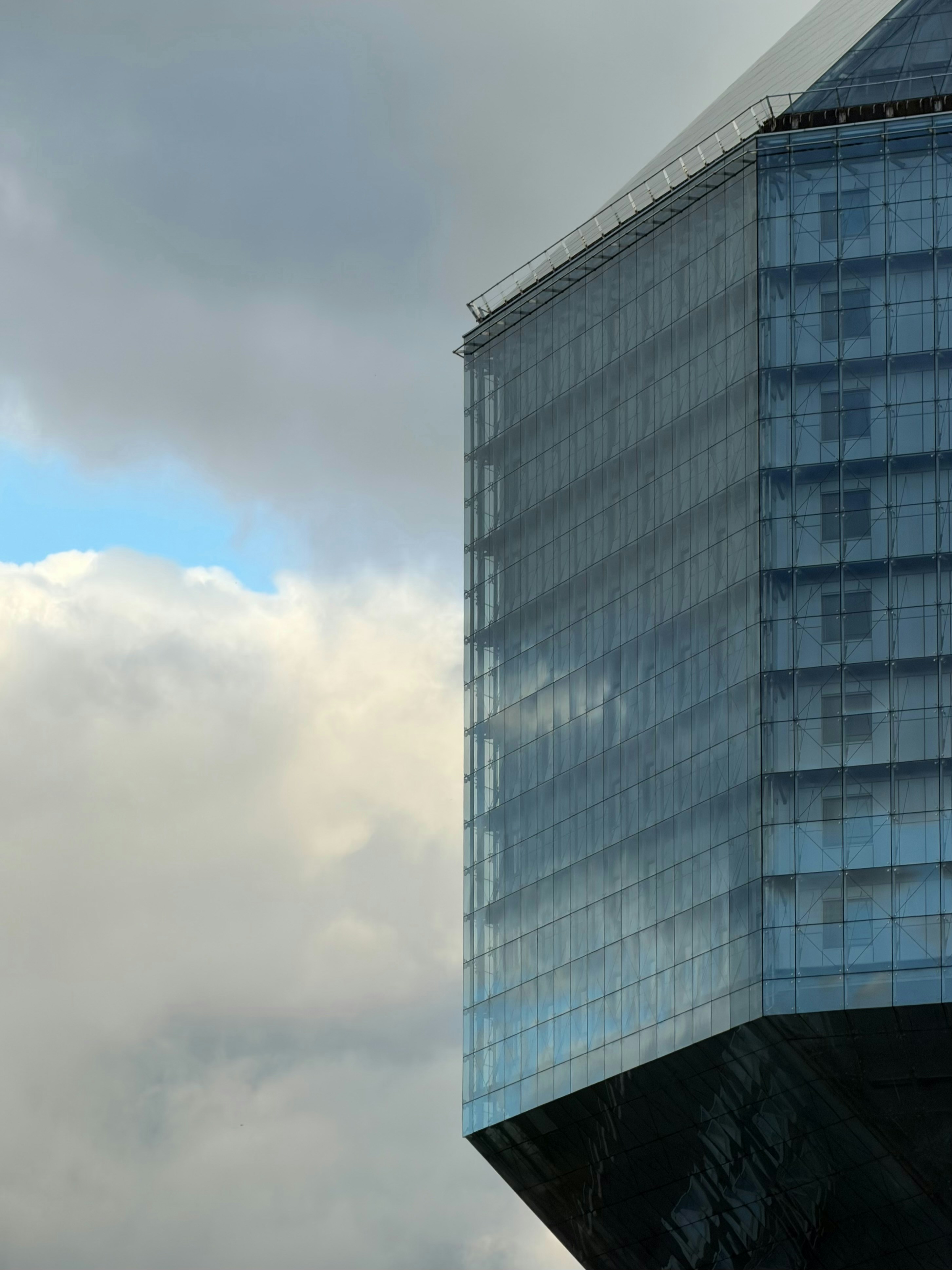 A modern glass skyscraper reflecting clouds against a blue and grey sky