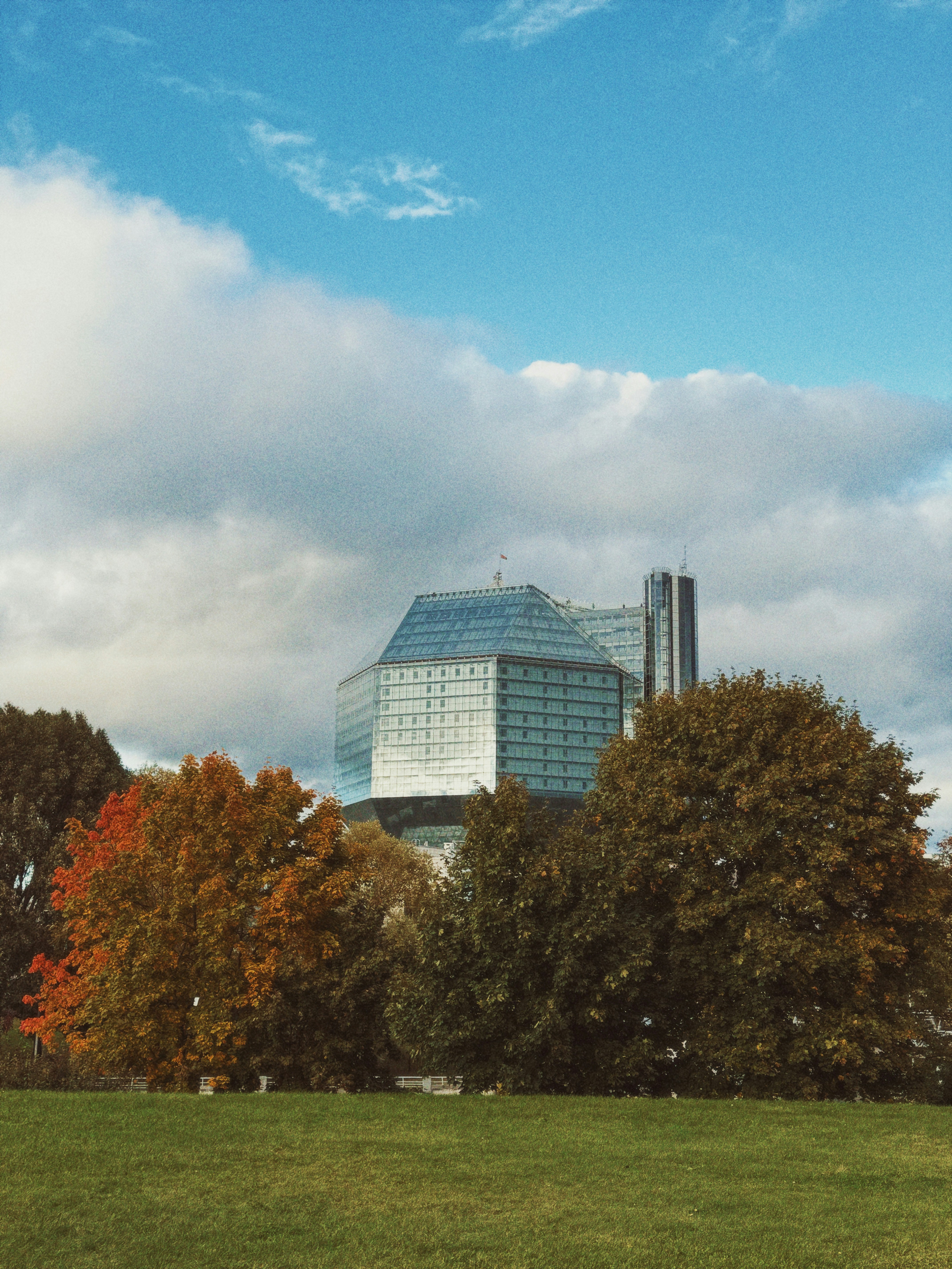 The National Library of Belarus behind autumn trees under a cloudy sky