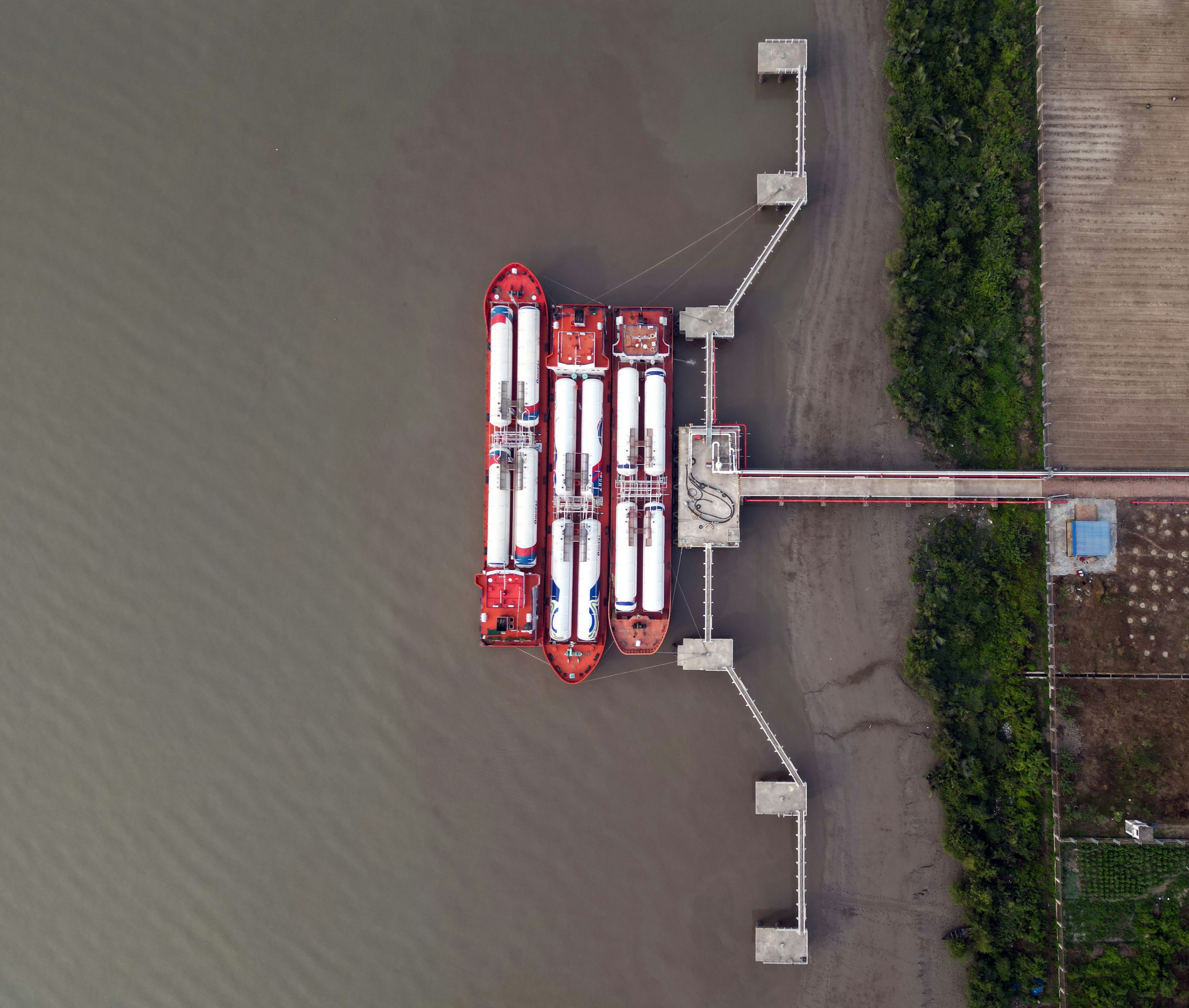 Vista aérea de três navios-tanque vermelhos atracados em um píer de concreto