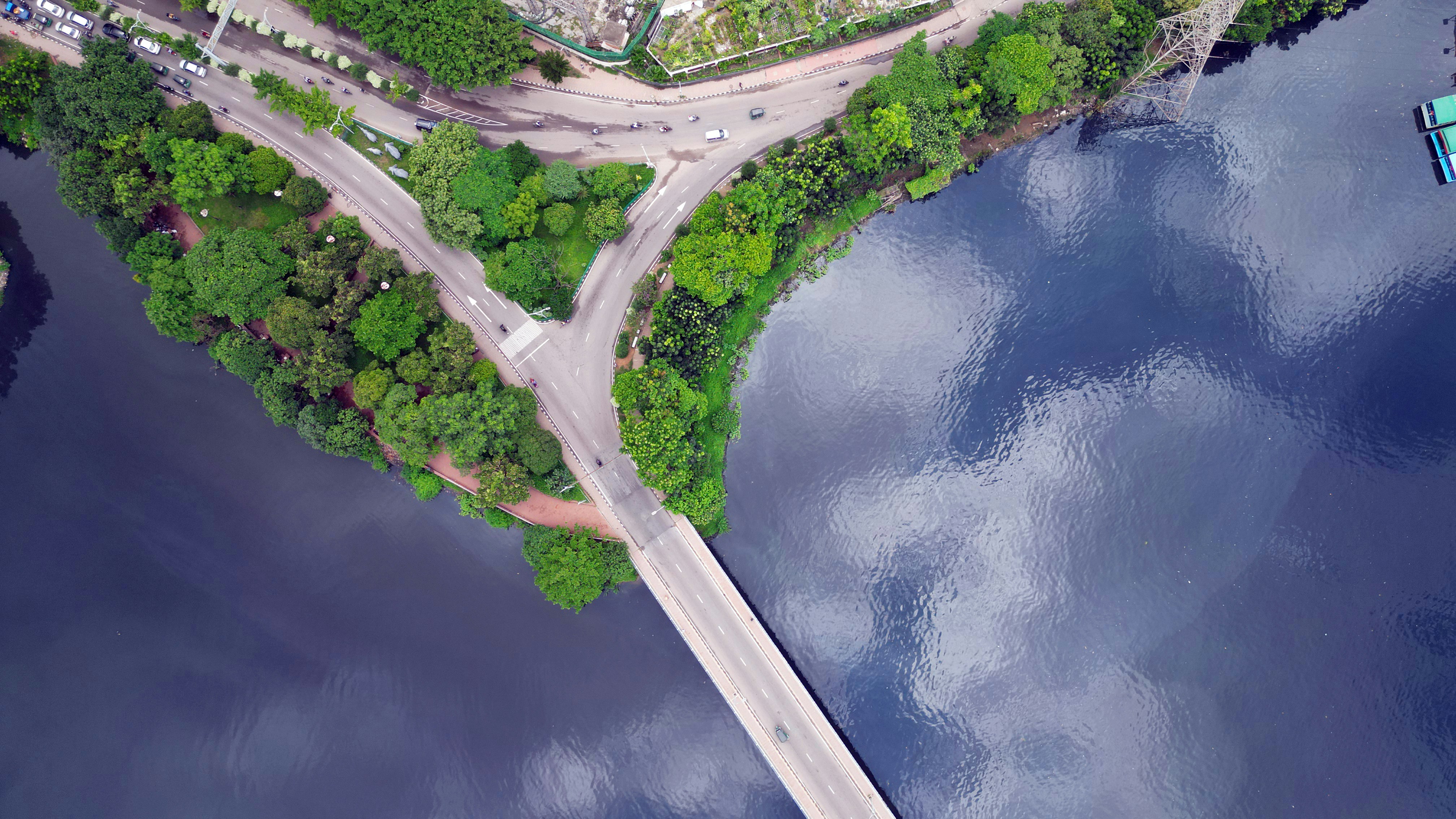 Uma vista aérea de uma ponte conectando uma estrada arborizada a um lago