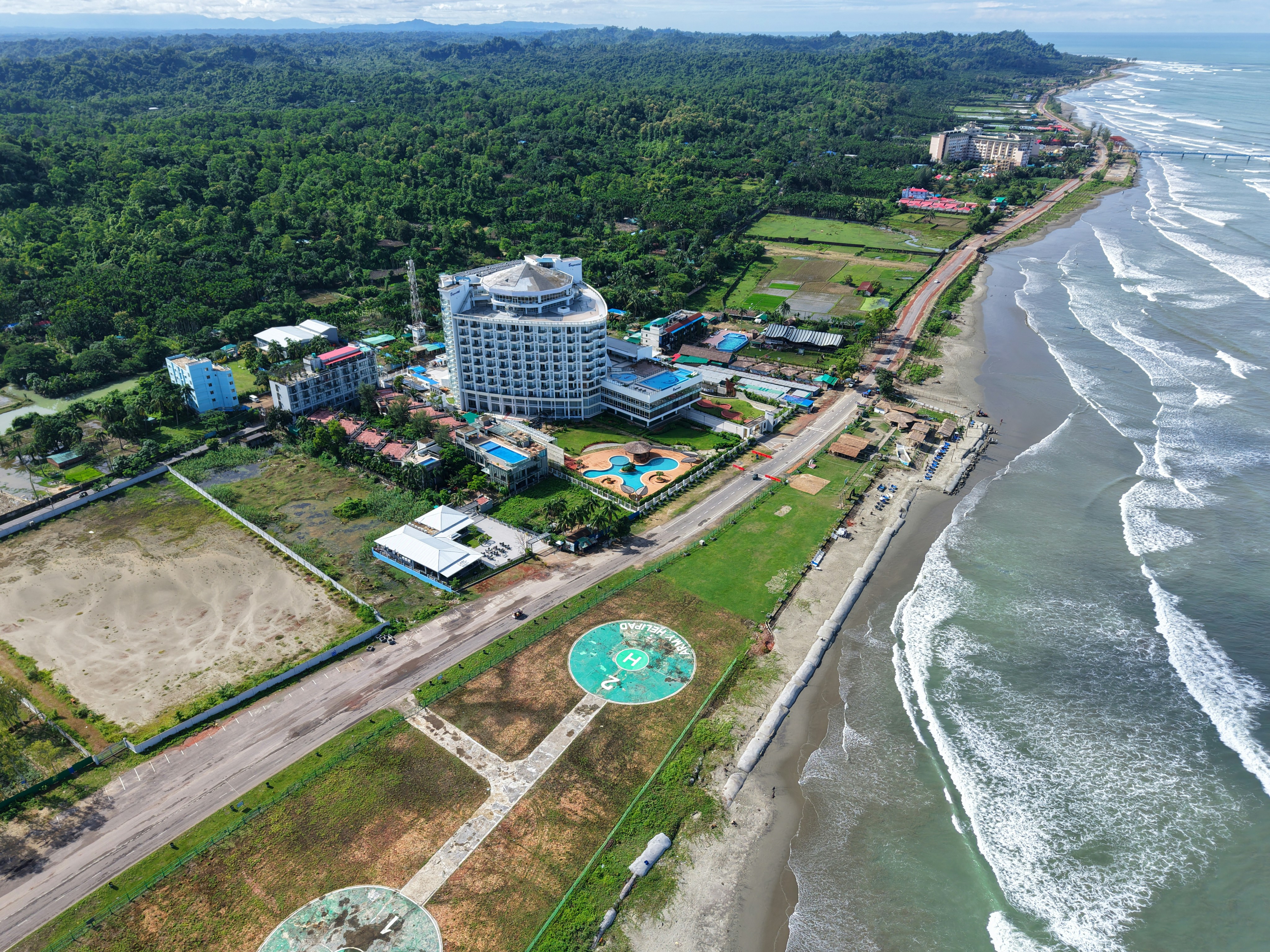 Uma vista aérea de um hotel costeiro com helipontos ao lado de uma praia de areia