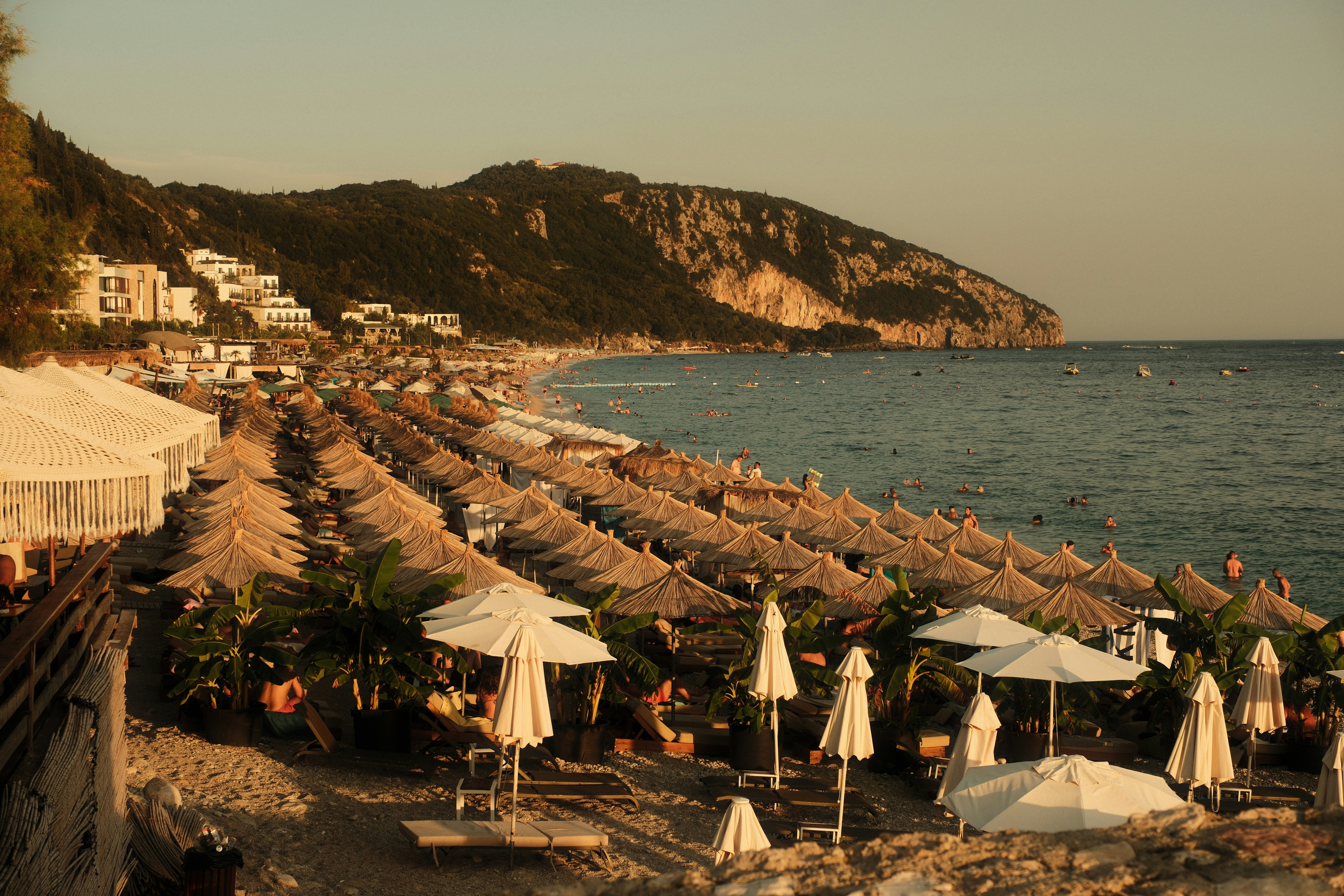 Rows of straw umbrellas on a beach with a mountain in the background