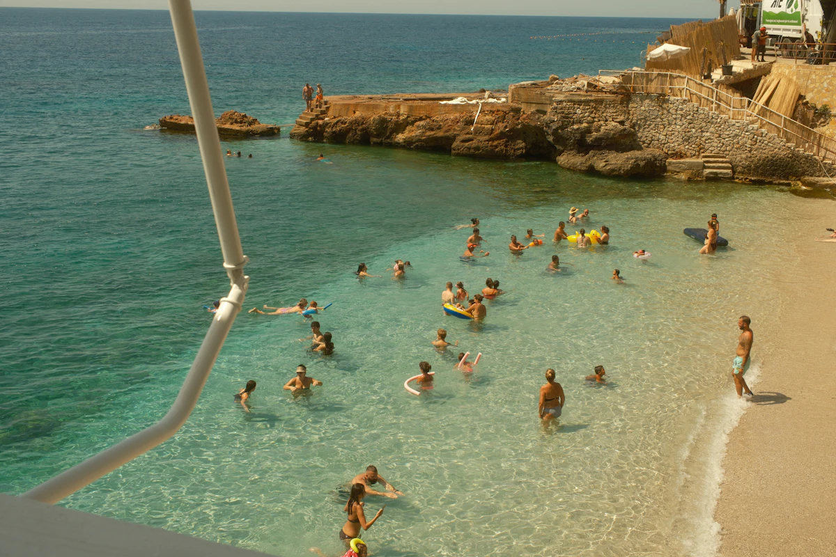 Swimmers in shallow turquoise water at a sandy cove beside rocks