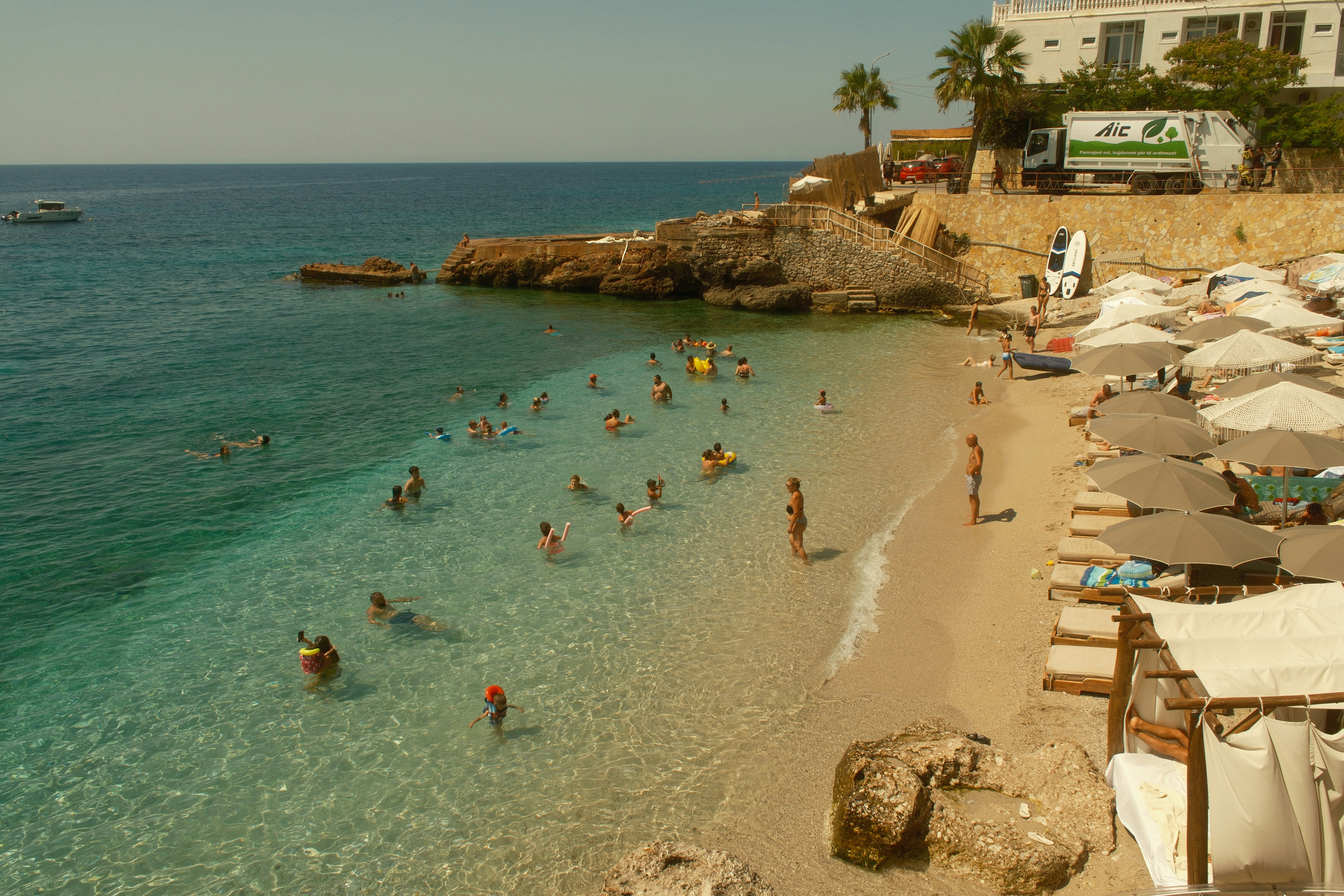 People swimming in clear turquoise water at a sandy beach with sun umbrellas