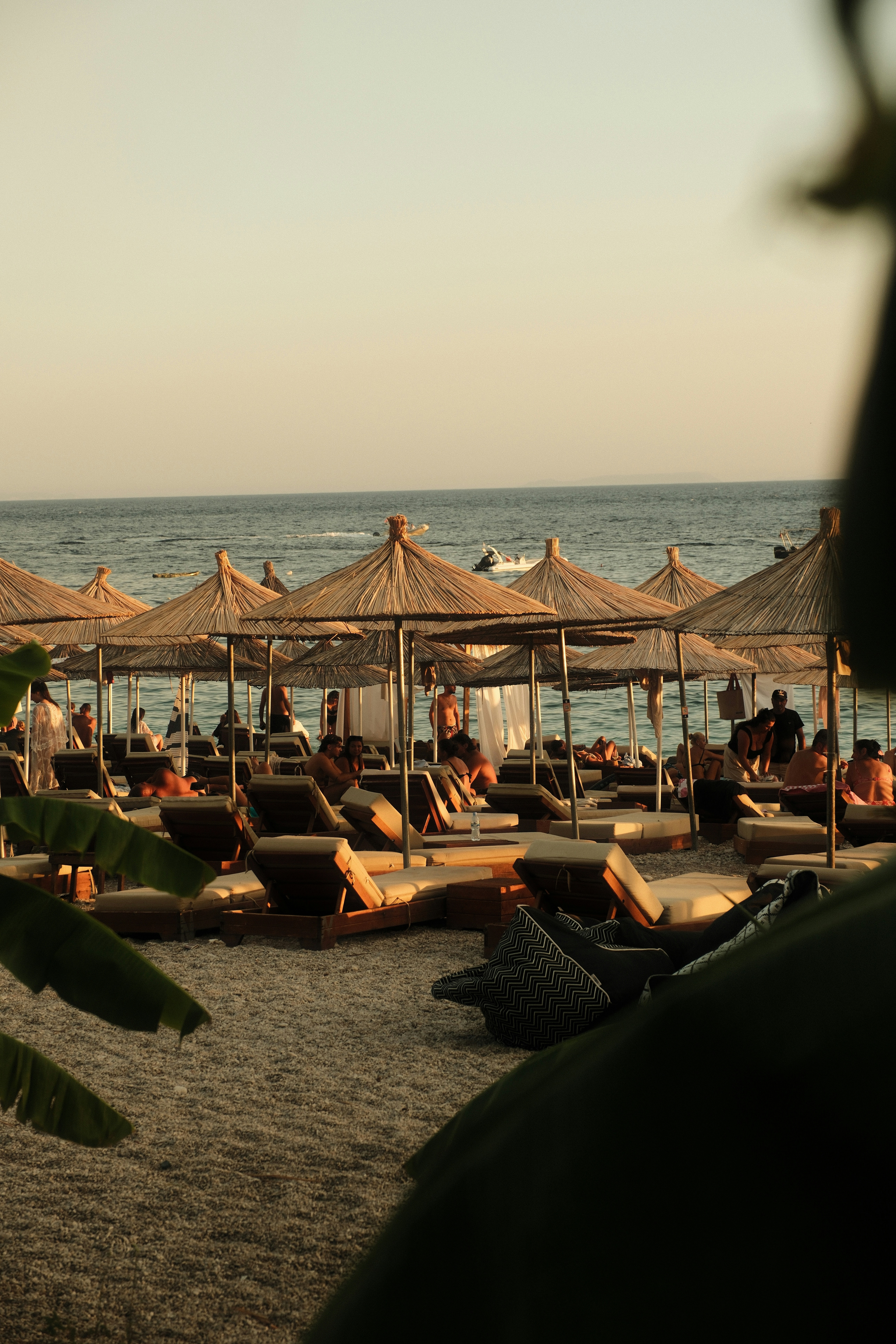 People relaxing on wooden lounge chairs under straw umbrellas on a pebble beach