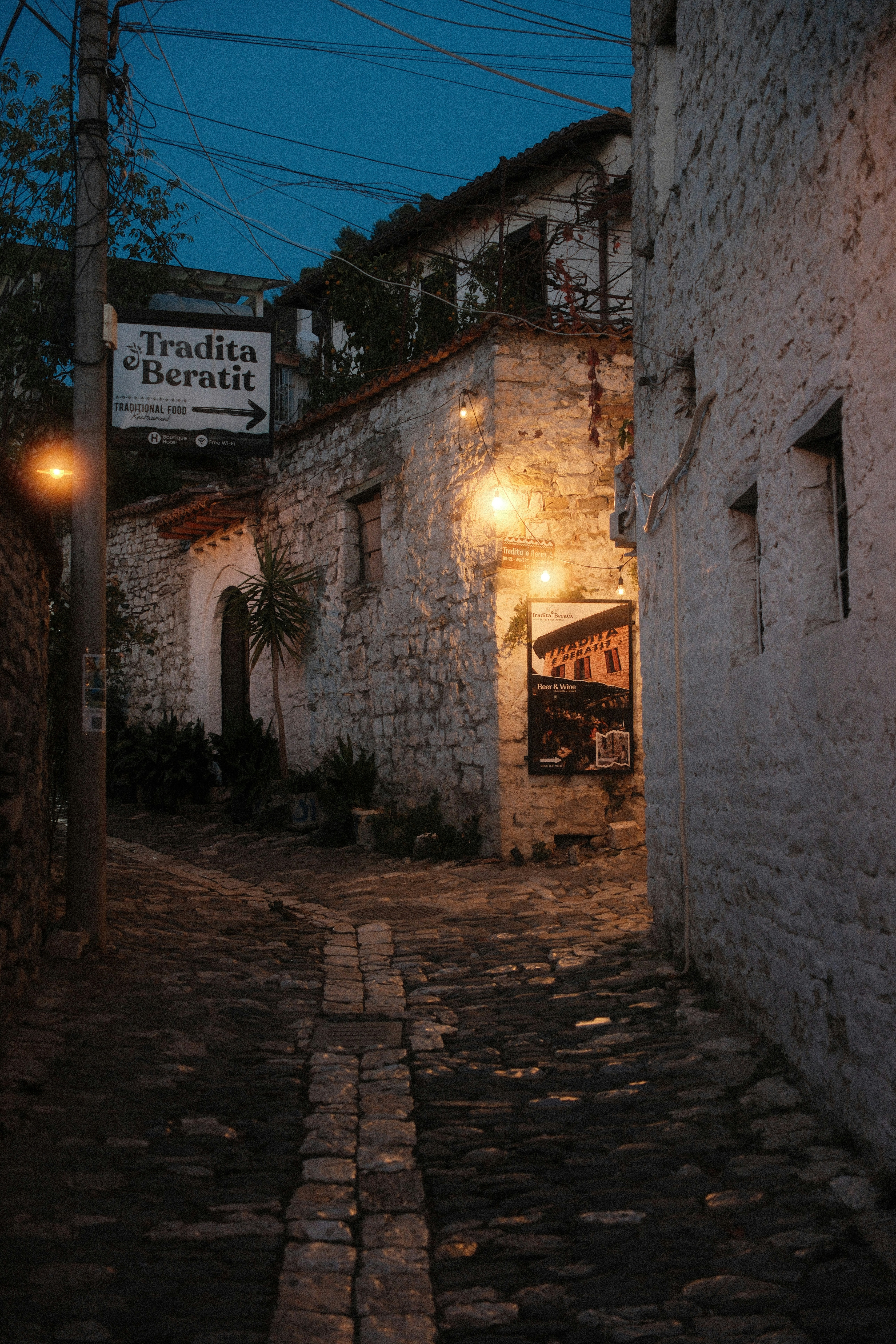 A narrow cobblestone street in Berat at night with illuminated stone buildings