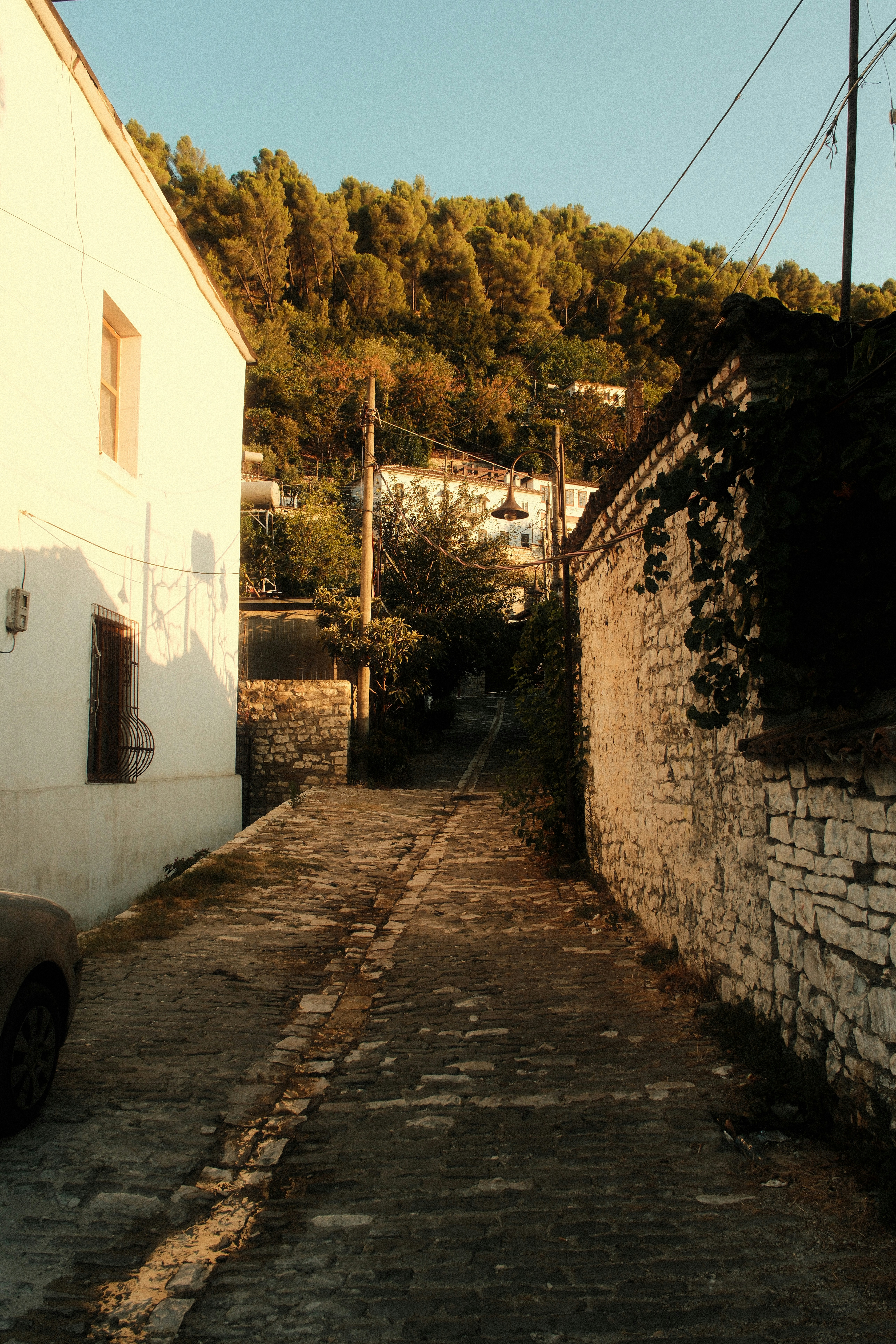 A narrow cobblestone street between a white building and a stone wall