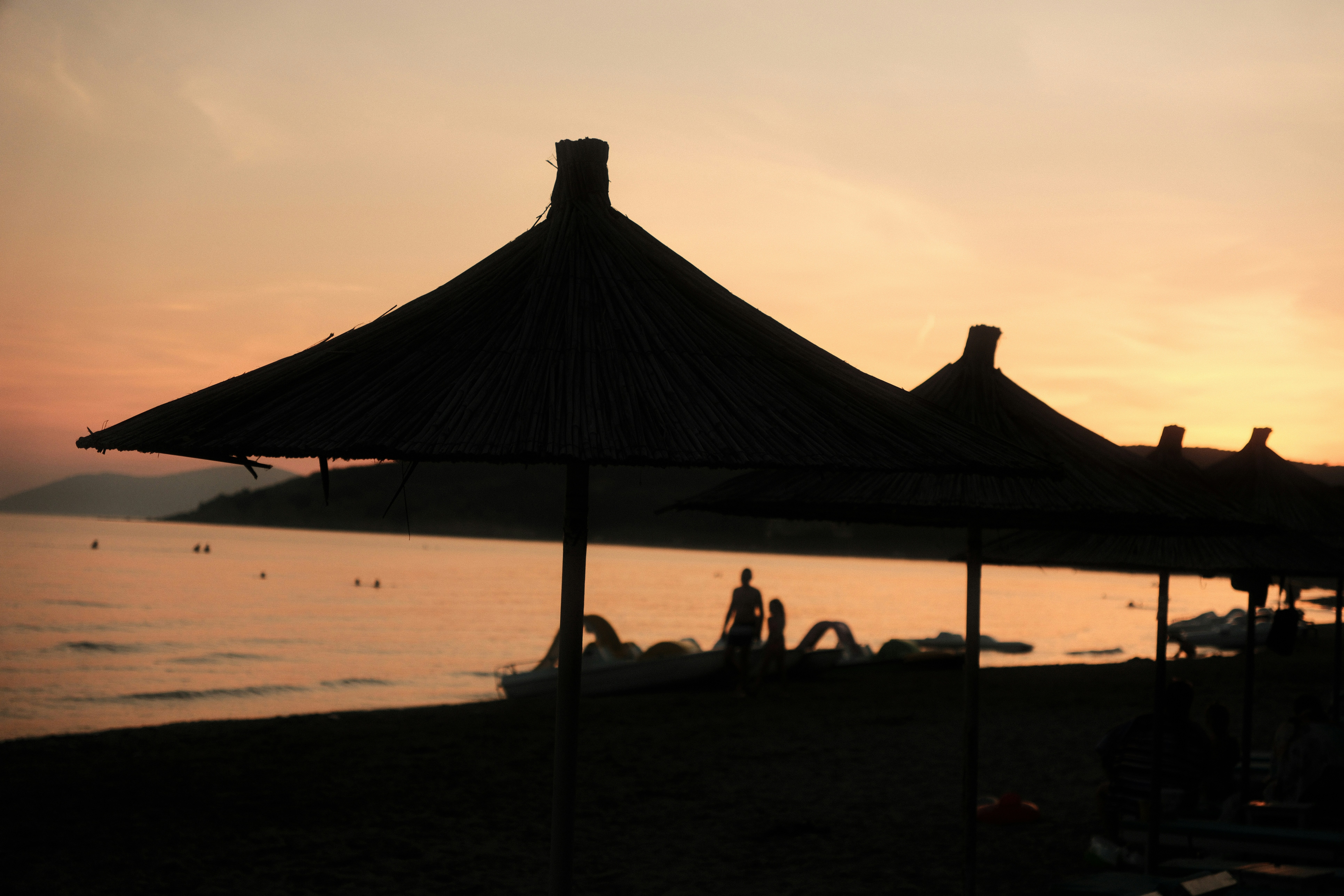 Straw beach umbrellas in silhouette against a warm orange sky over the sea