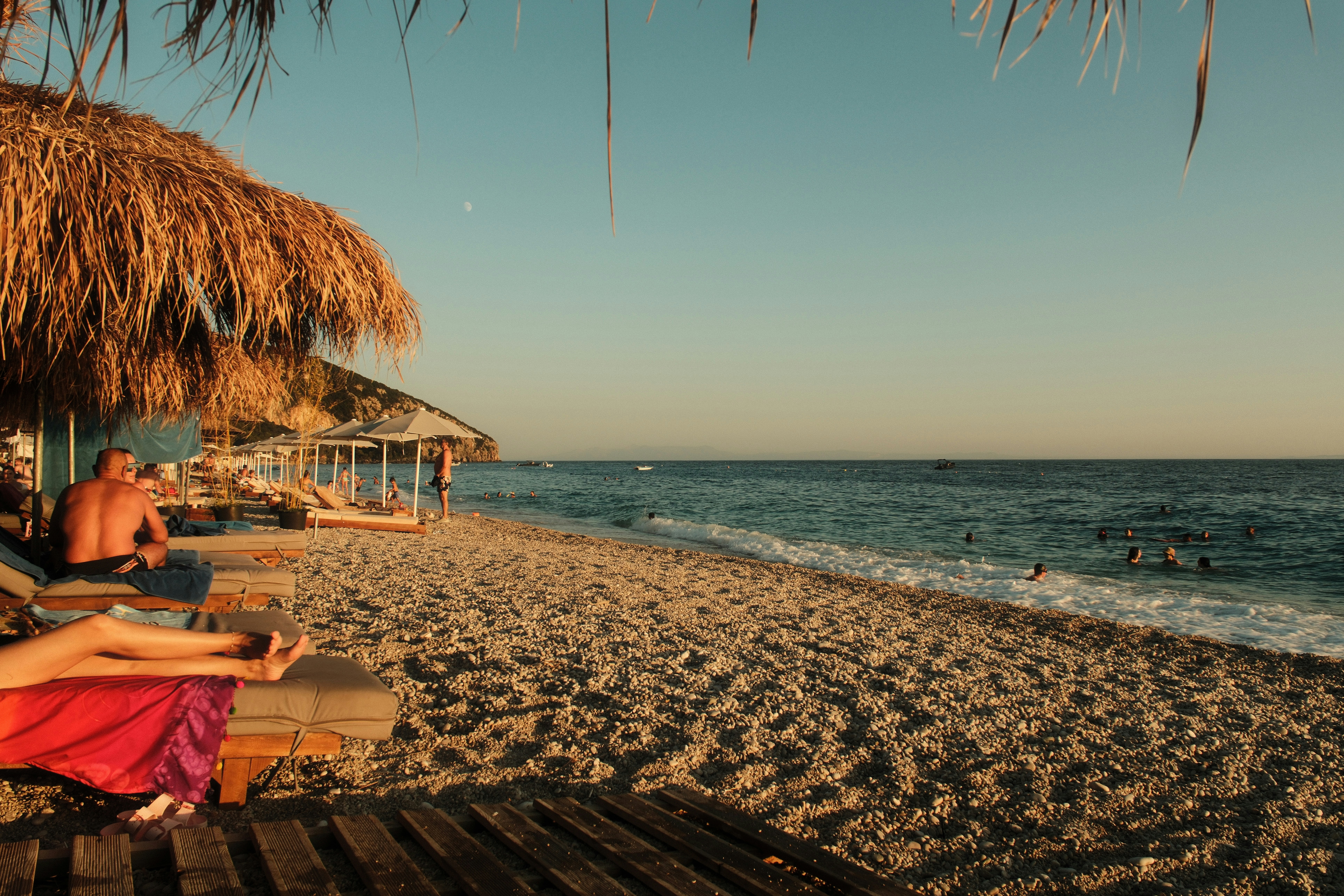 People relaxing on lounge chairs under straw umbrellas on a pebble beach