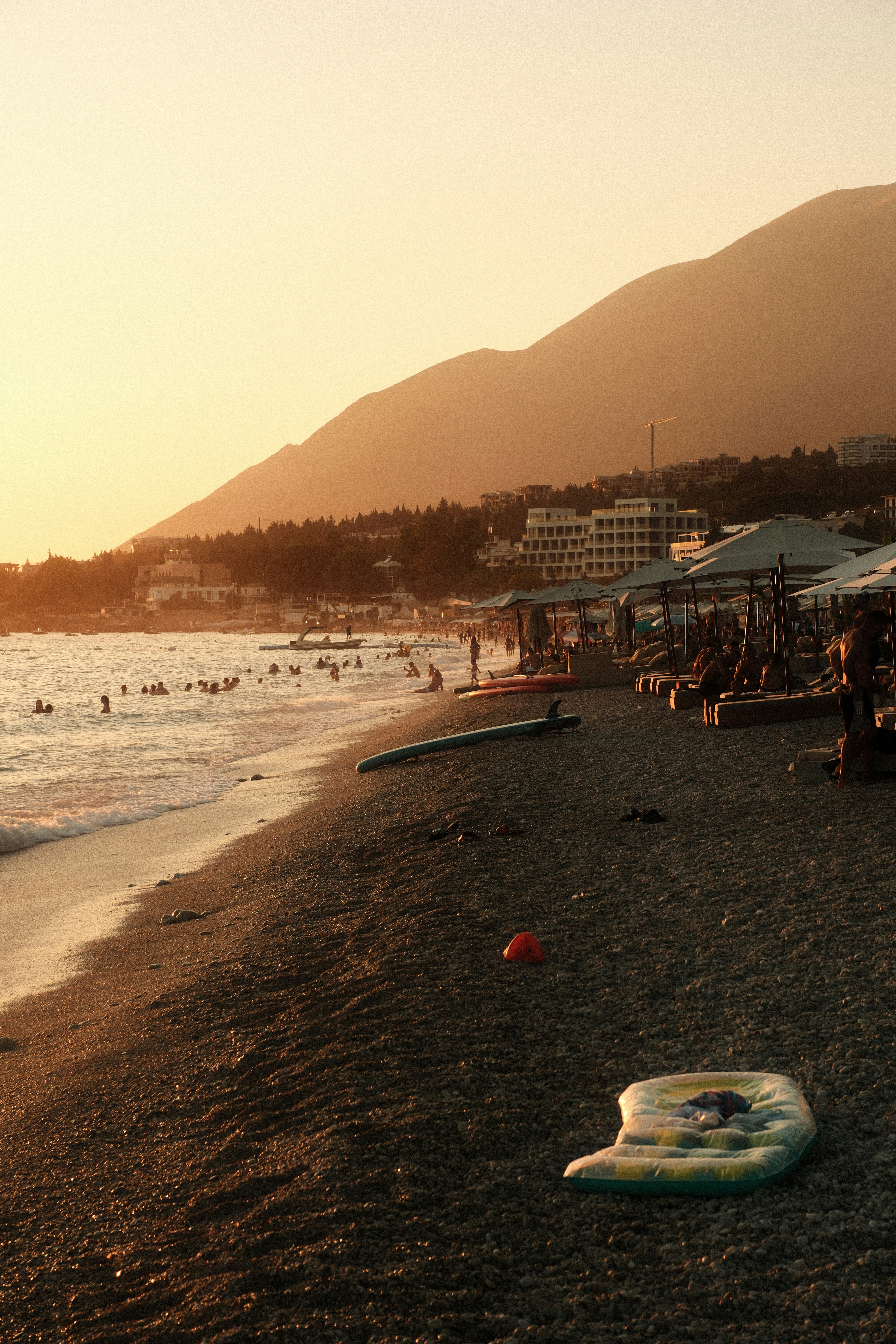 People swimming and relaxing on a pebble beach during the golden hour