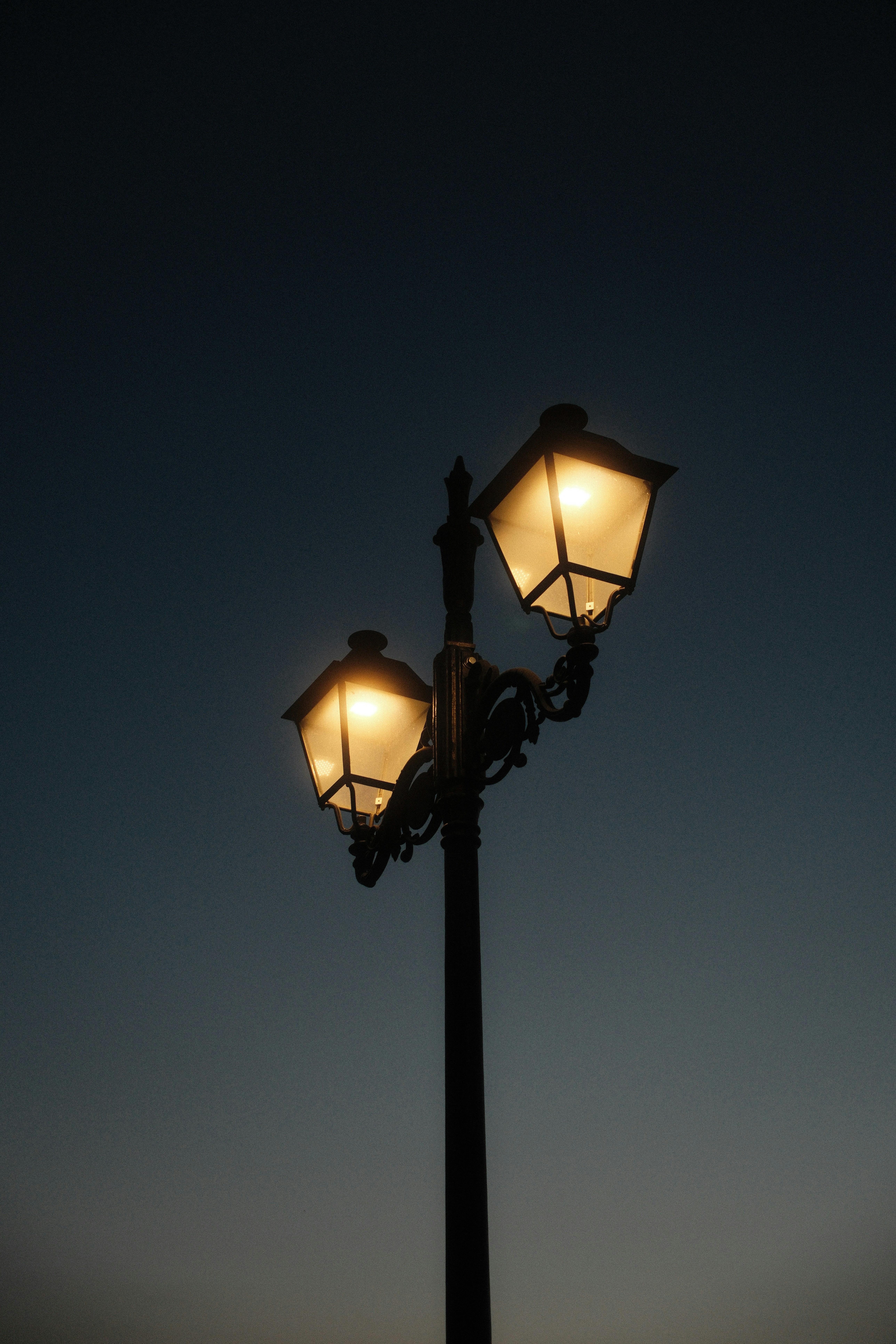 A black metal street lamp with two glowing lanterns against a dark sky