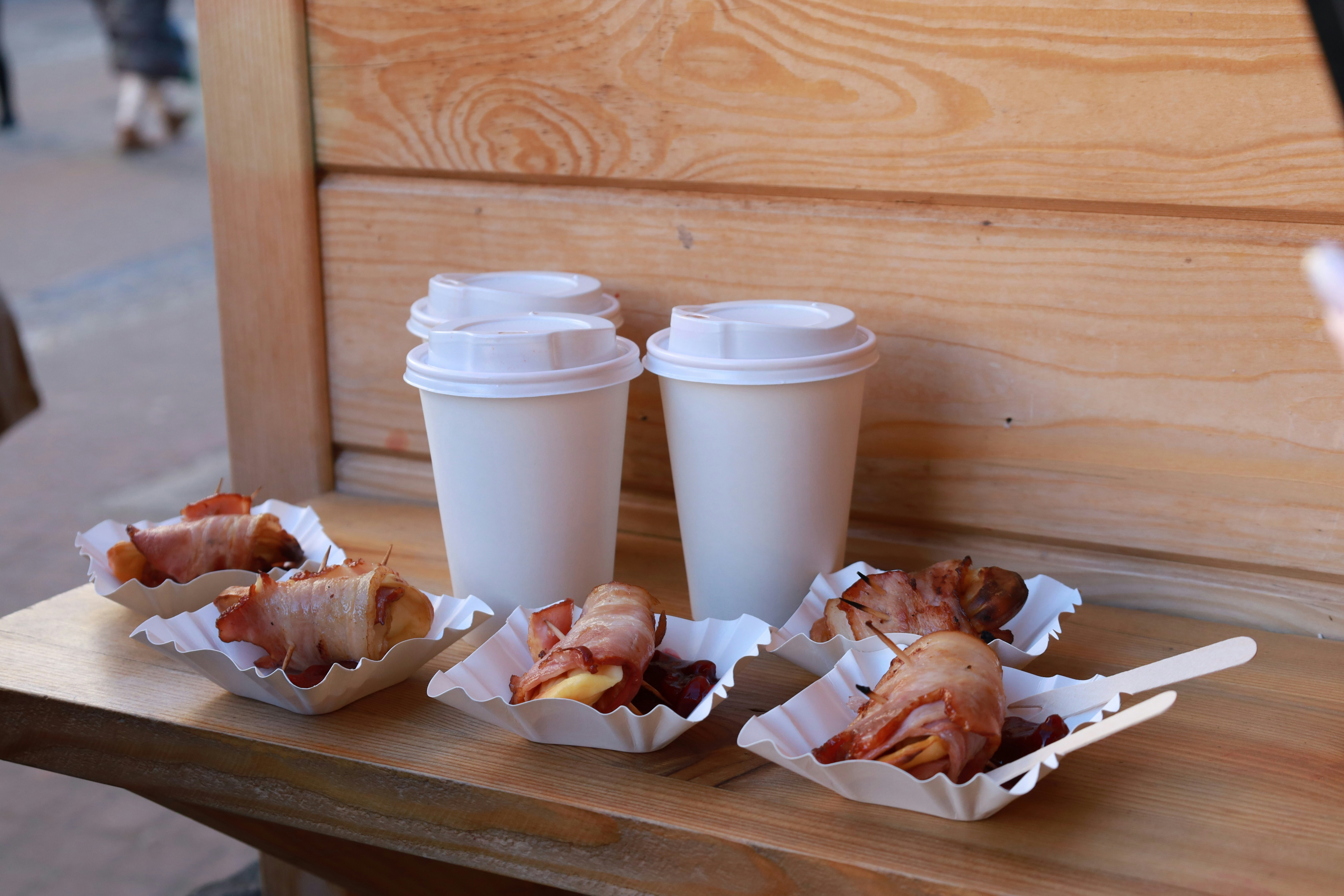 Coffee cups beside wrapped bacon rolls