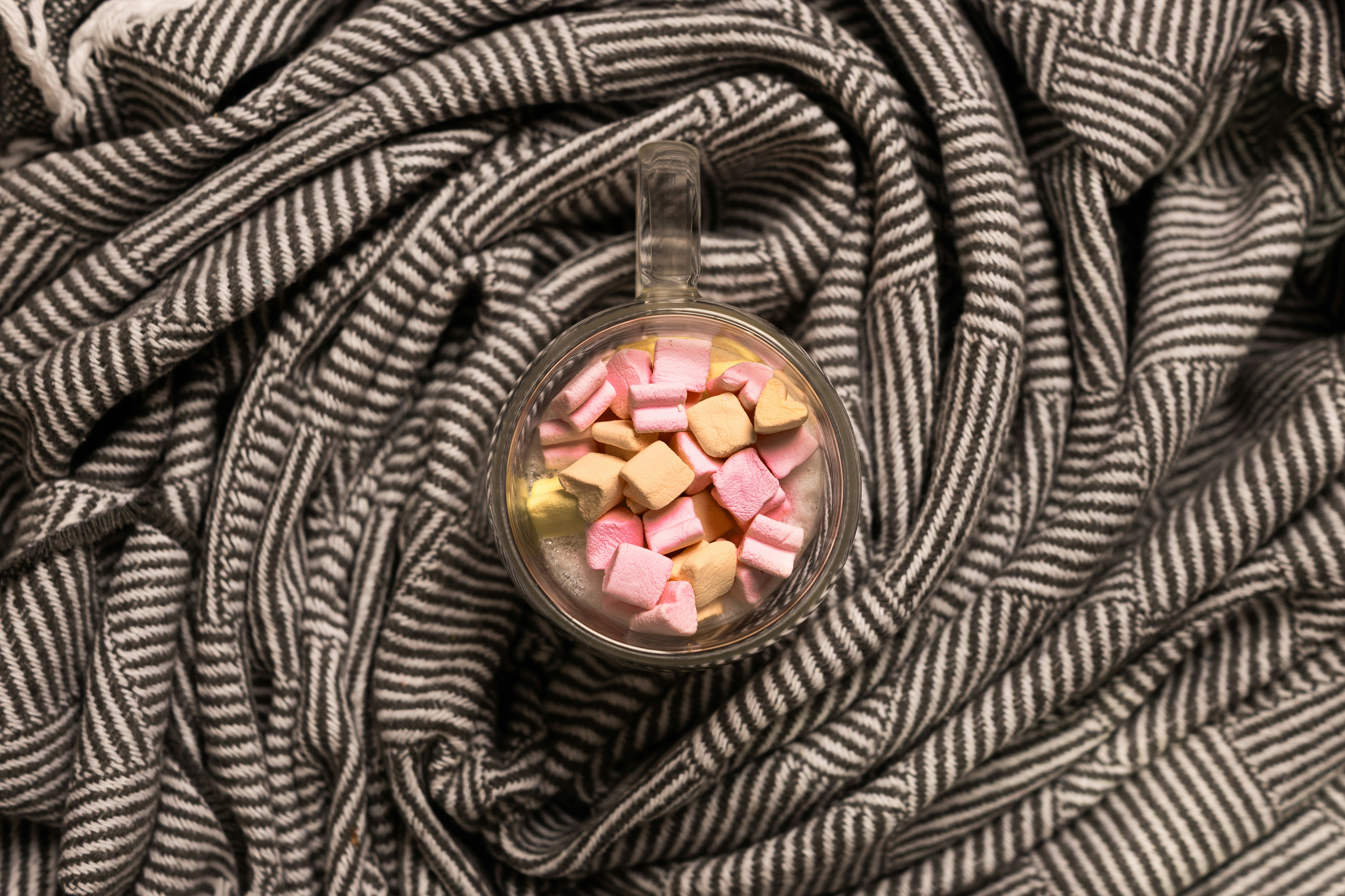 Glass mug of hot cocoa with marshmallows on a striped blanket