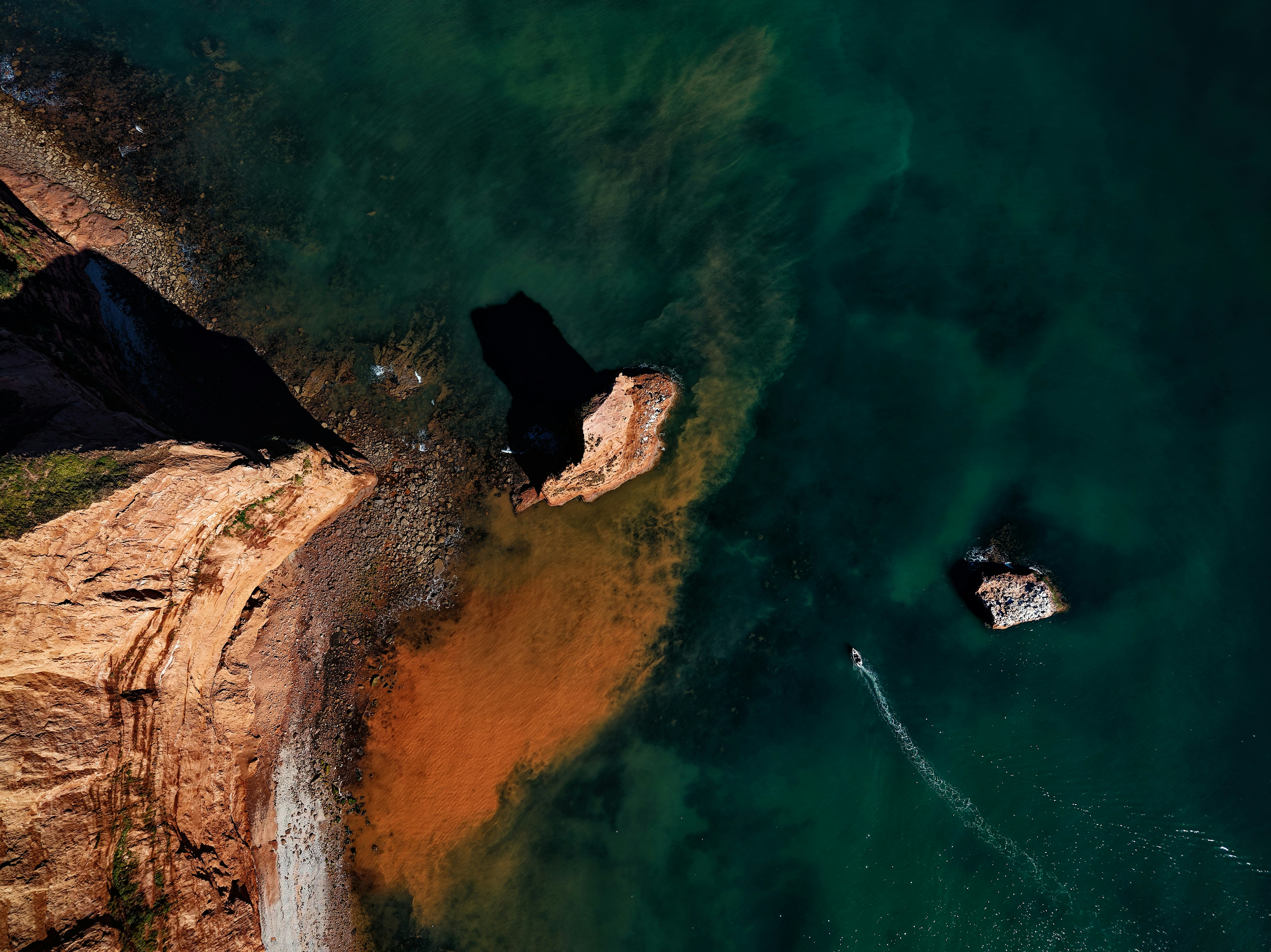 Aerial view of red sandstone cliffs and sediment in the sea at Sidmouth