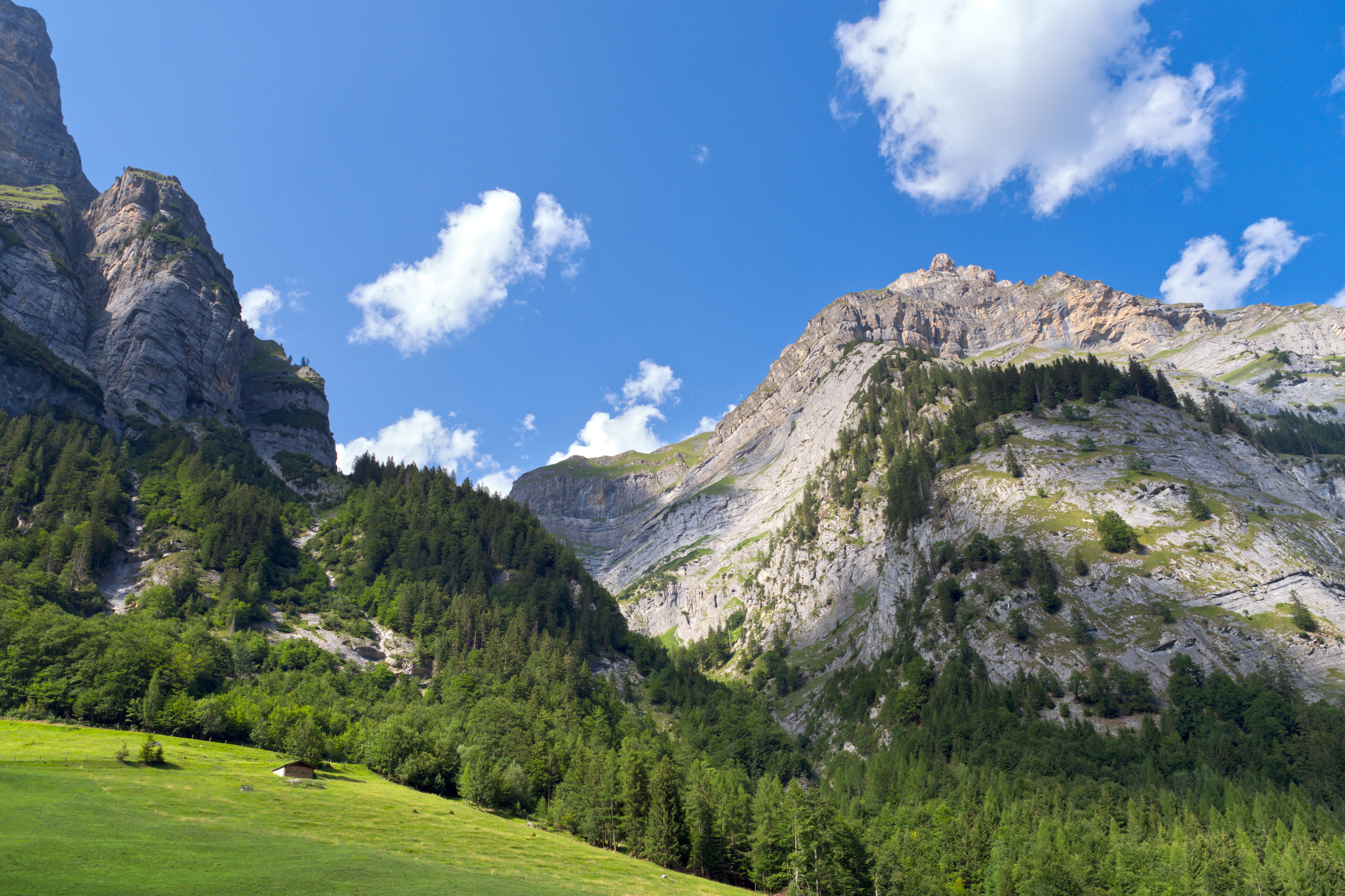 A small wooden hut on a green mountain meadow below steep rocky cliffs