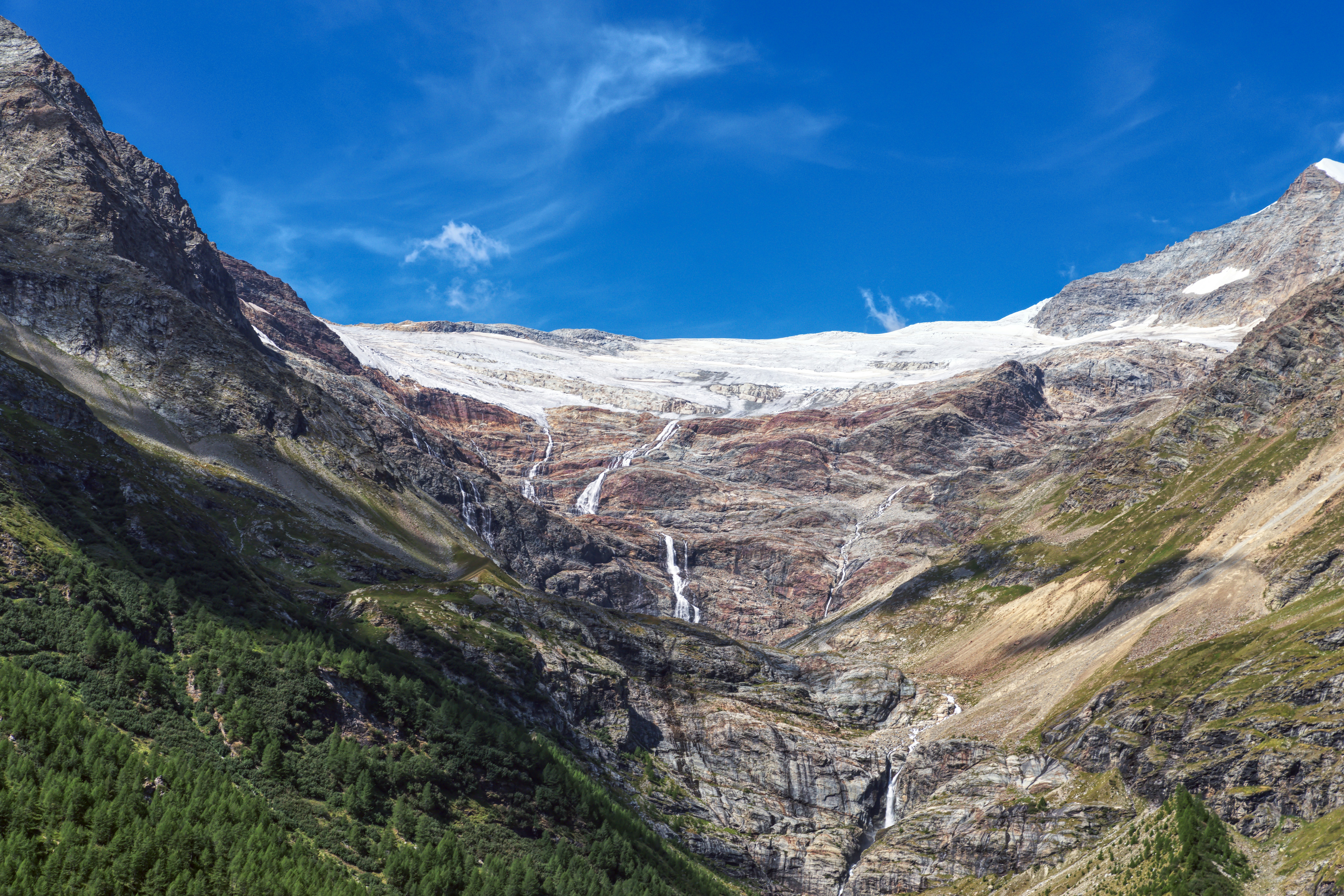 Glacial meltwater cascading down a steep rocky mountain face under a blue sky