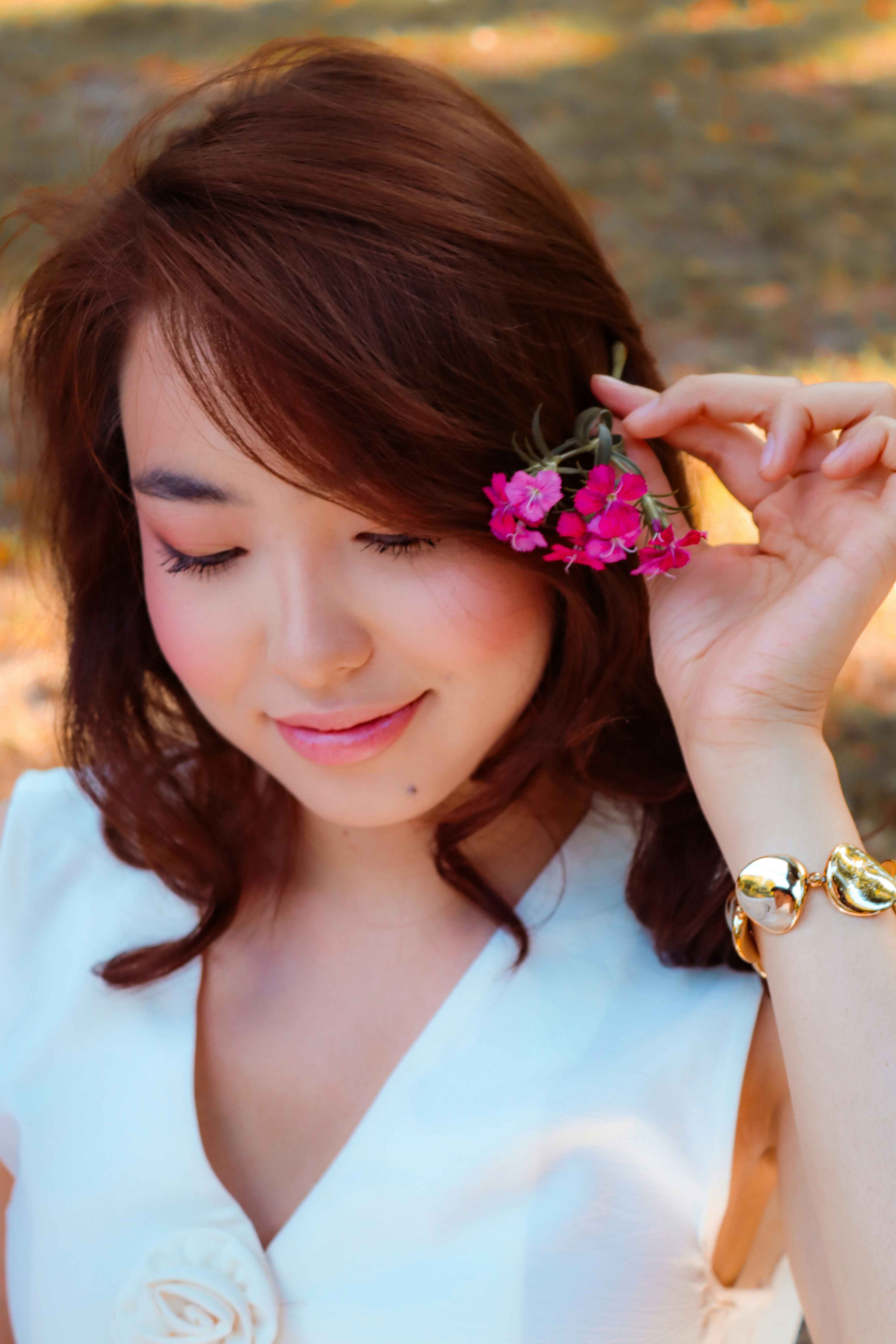 A woman with brown hair holding small pink flowers near her face