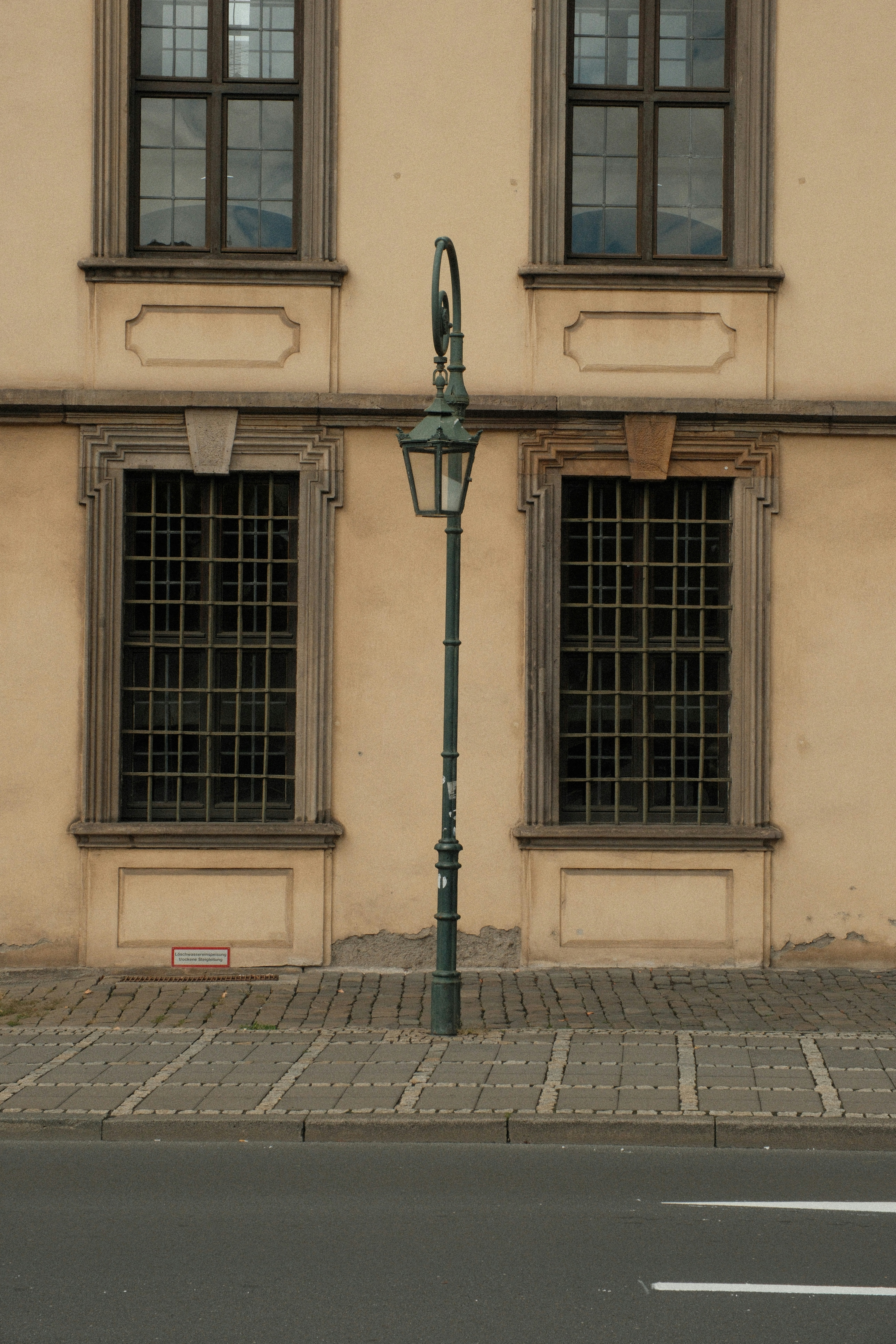A vintage street lamp between two windows with iron grilles on a beige building