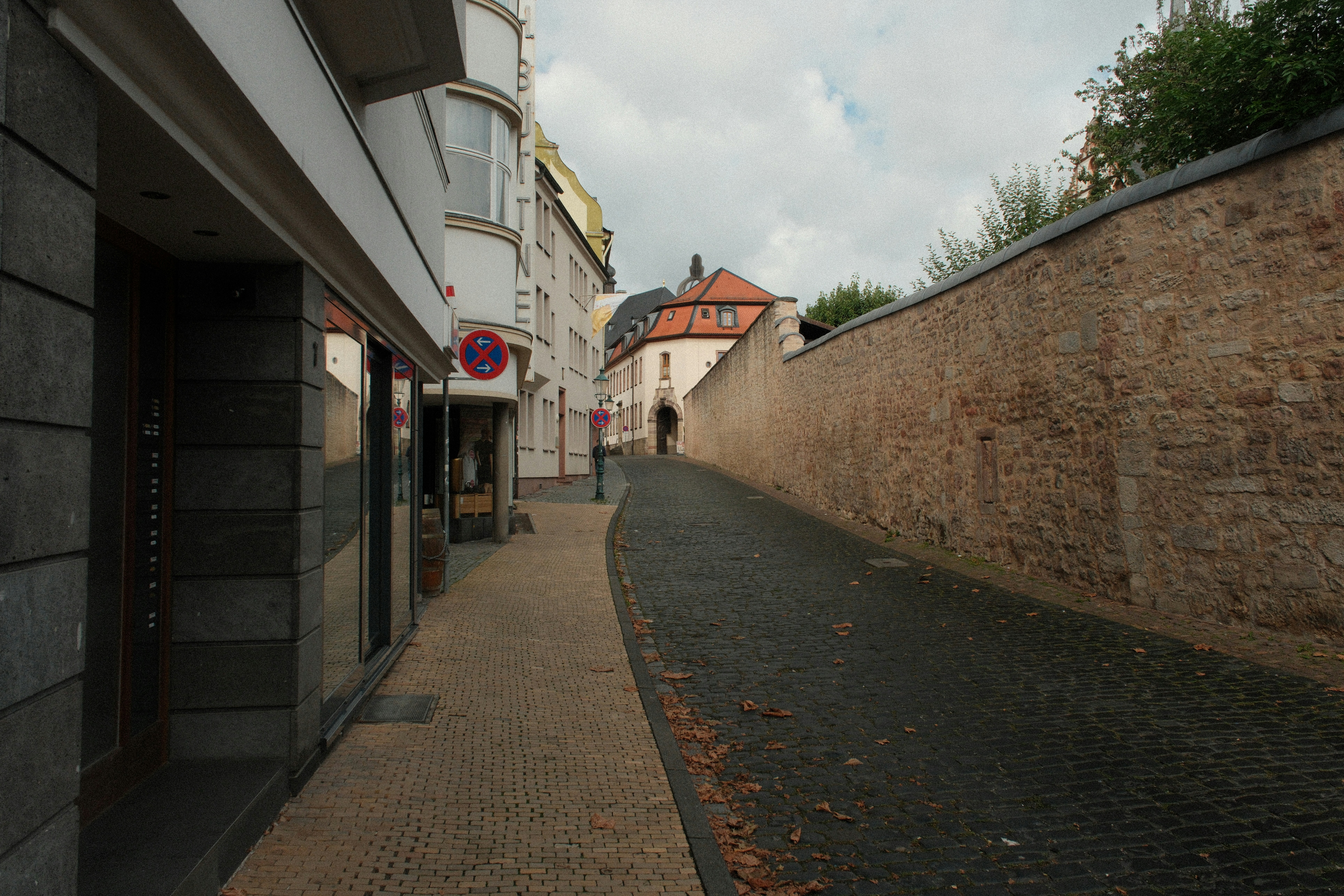 A cobblestone street beside a tall stone wall and white buildings