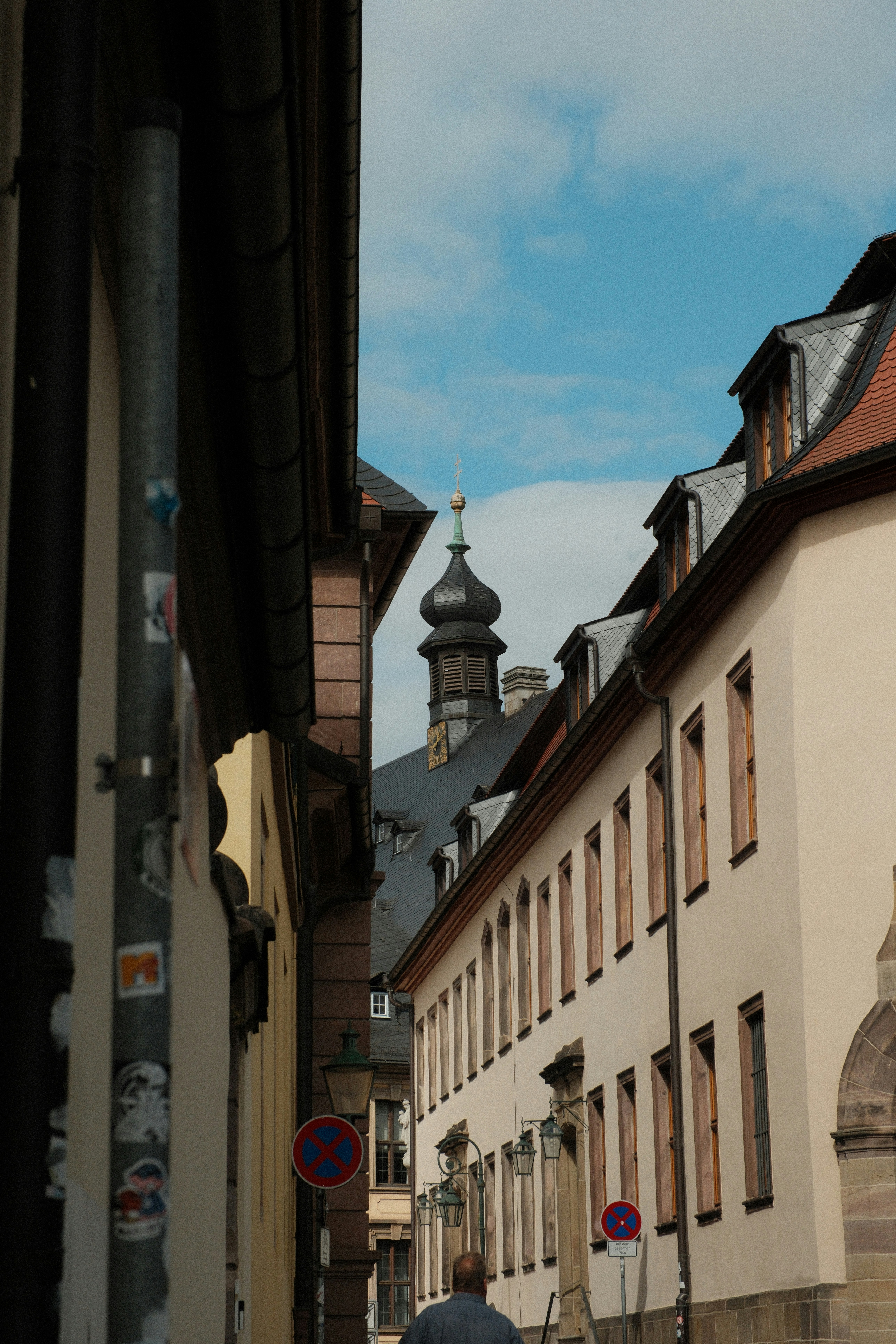 A narrow street between historic buildings with a church tower in the distance