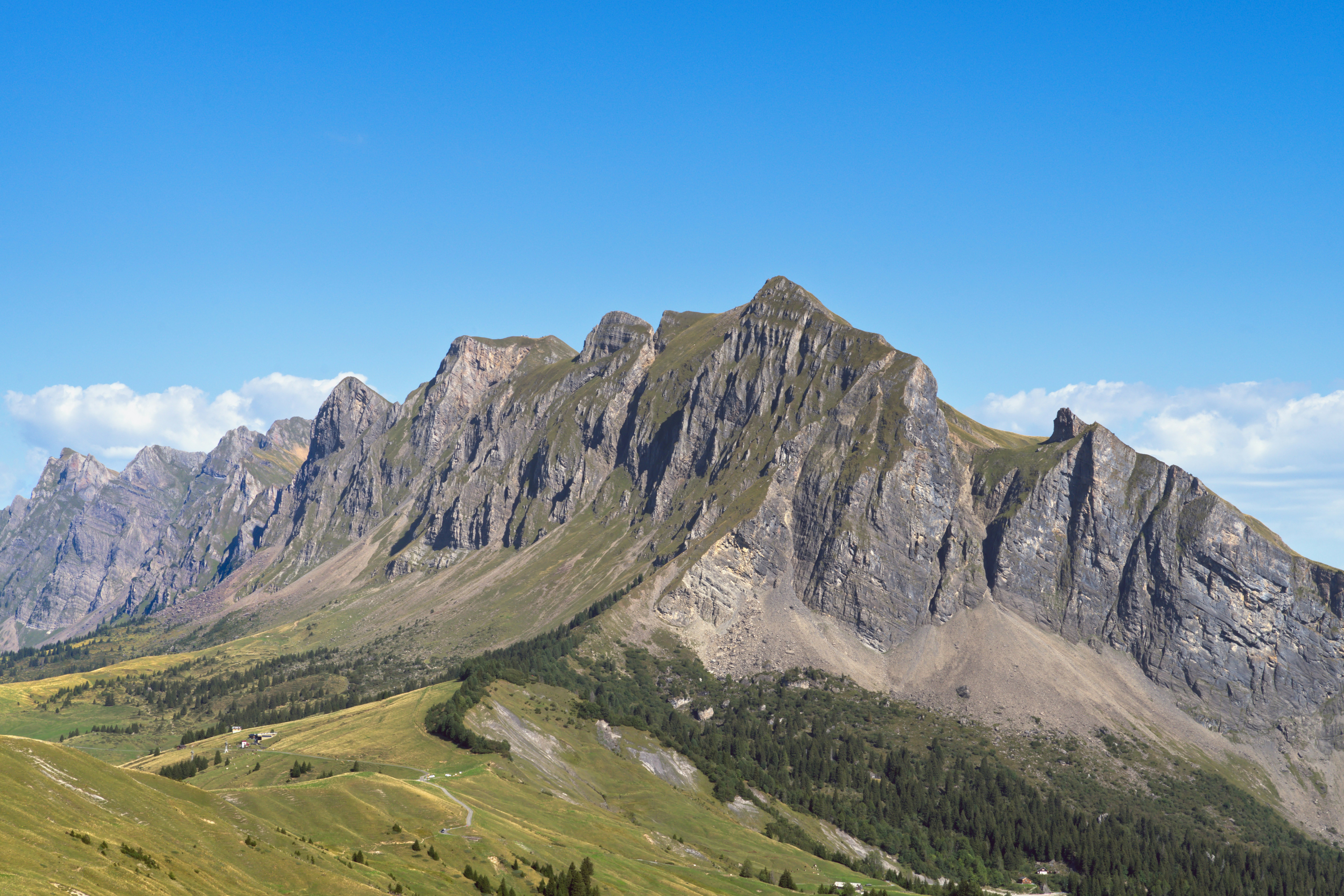 Jagged rocky mountain peaks rising above green alpine slopes under a clear blue sky