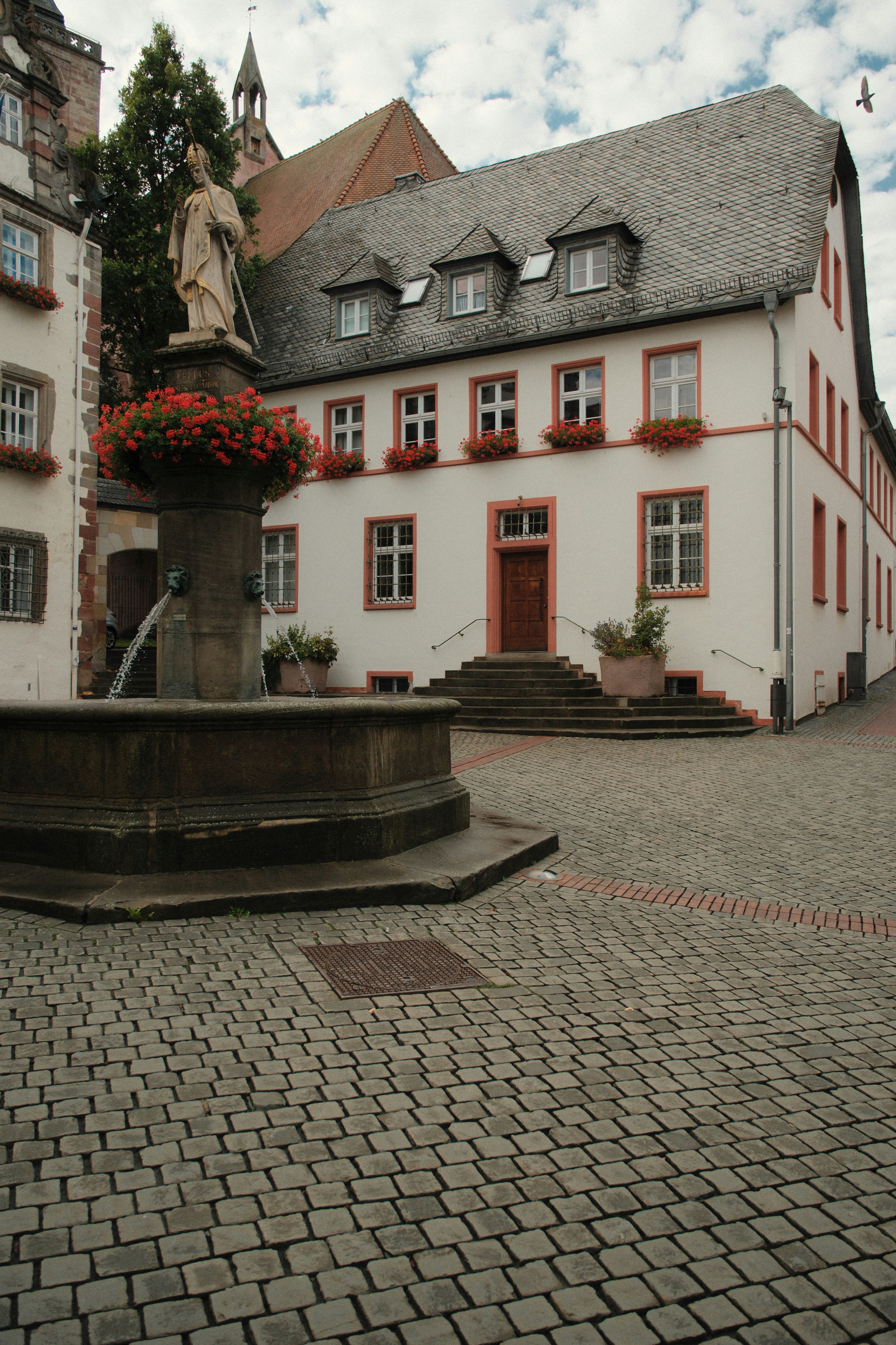 A stone fountain with a statue in a cobblestone square with white buildings