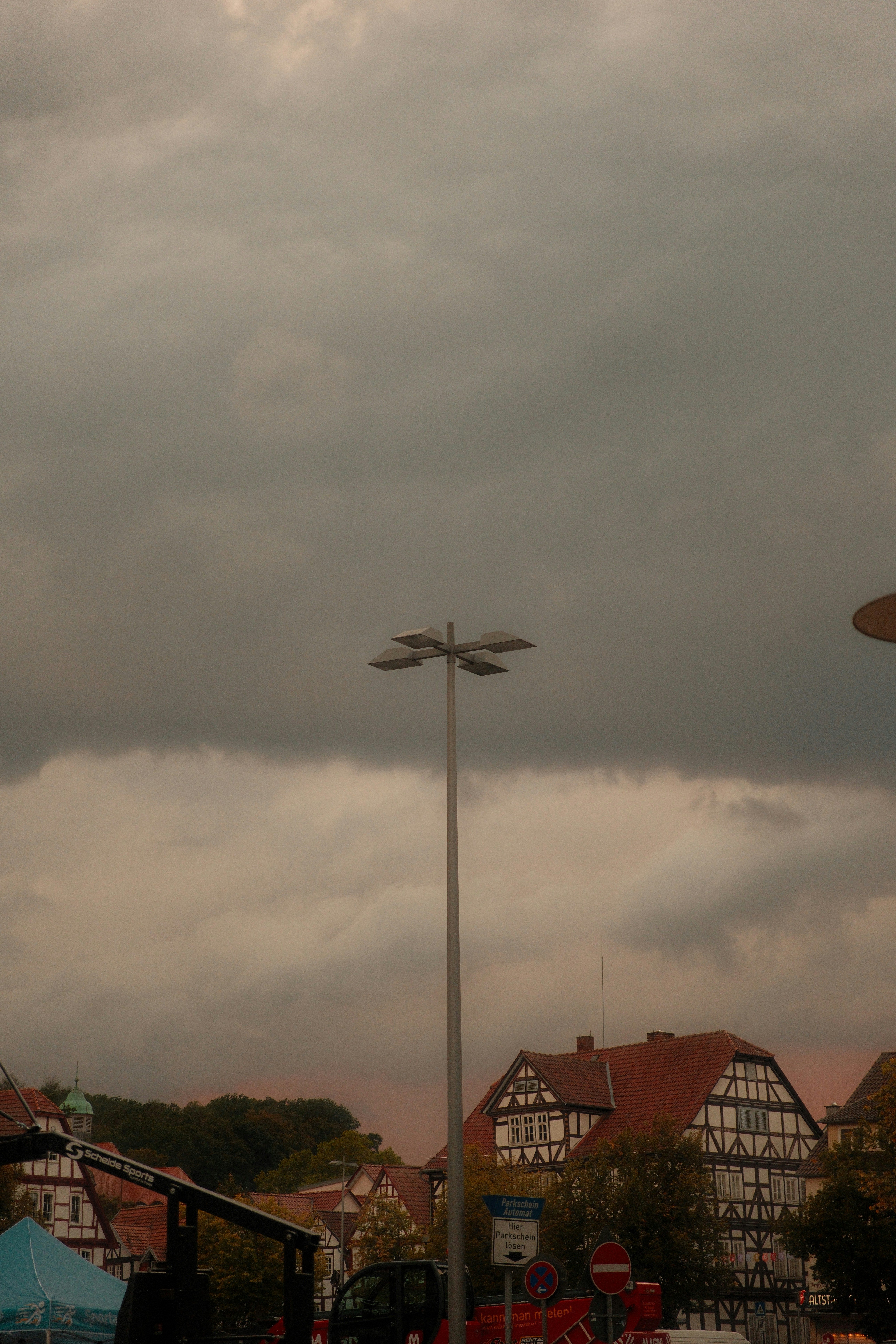 A tall light pole against a dark, overcast sky above traditional timber-framed houses
