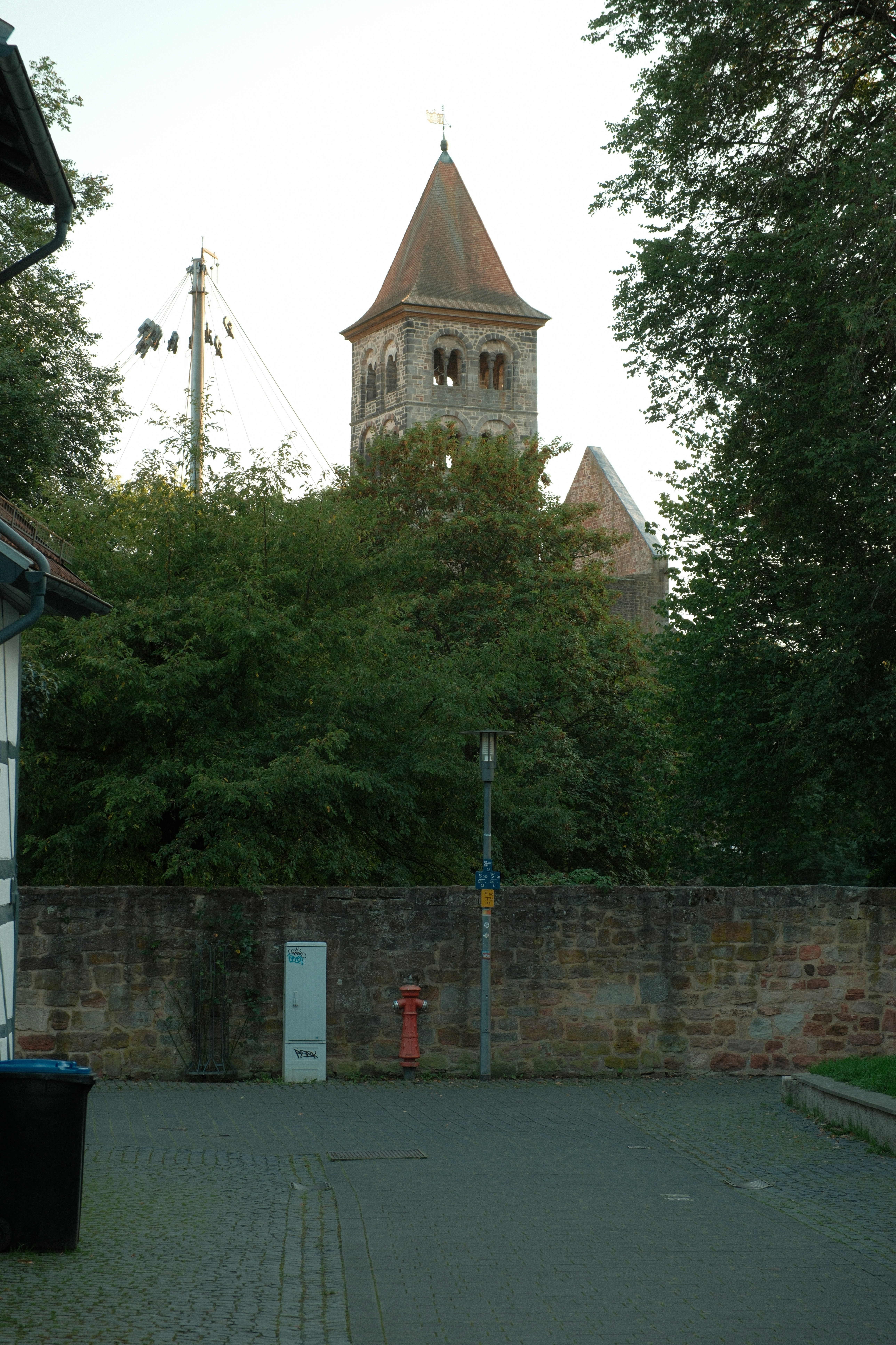 A stone church tower rising above dense green trees behind a stone wall