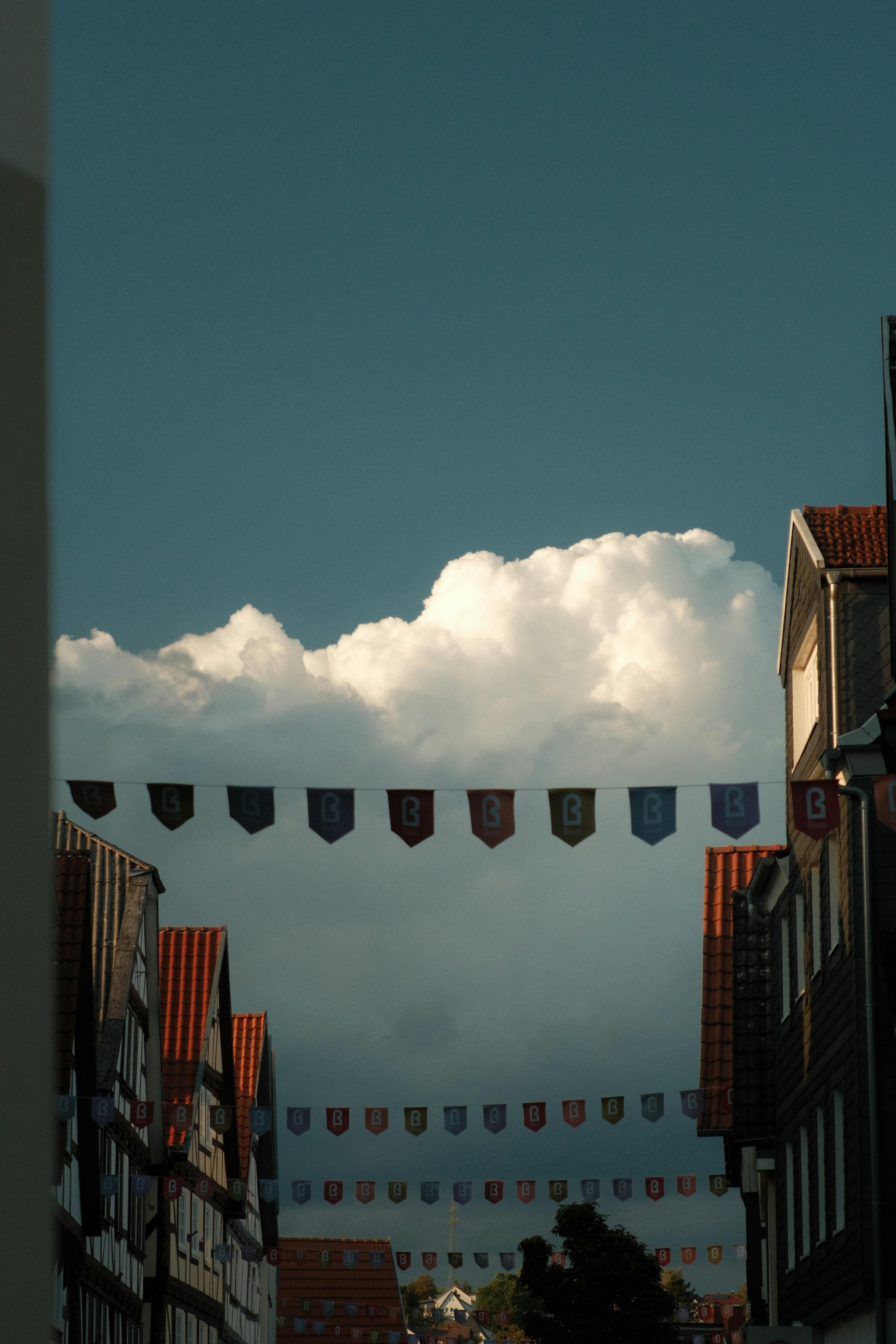 Rows of colorful pennant flags strung between traditional timber-framed houses under a cloudy sky