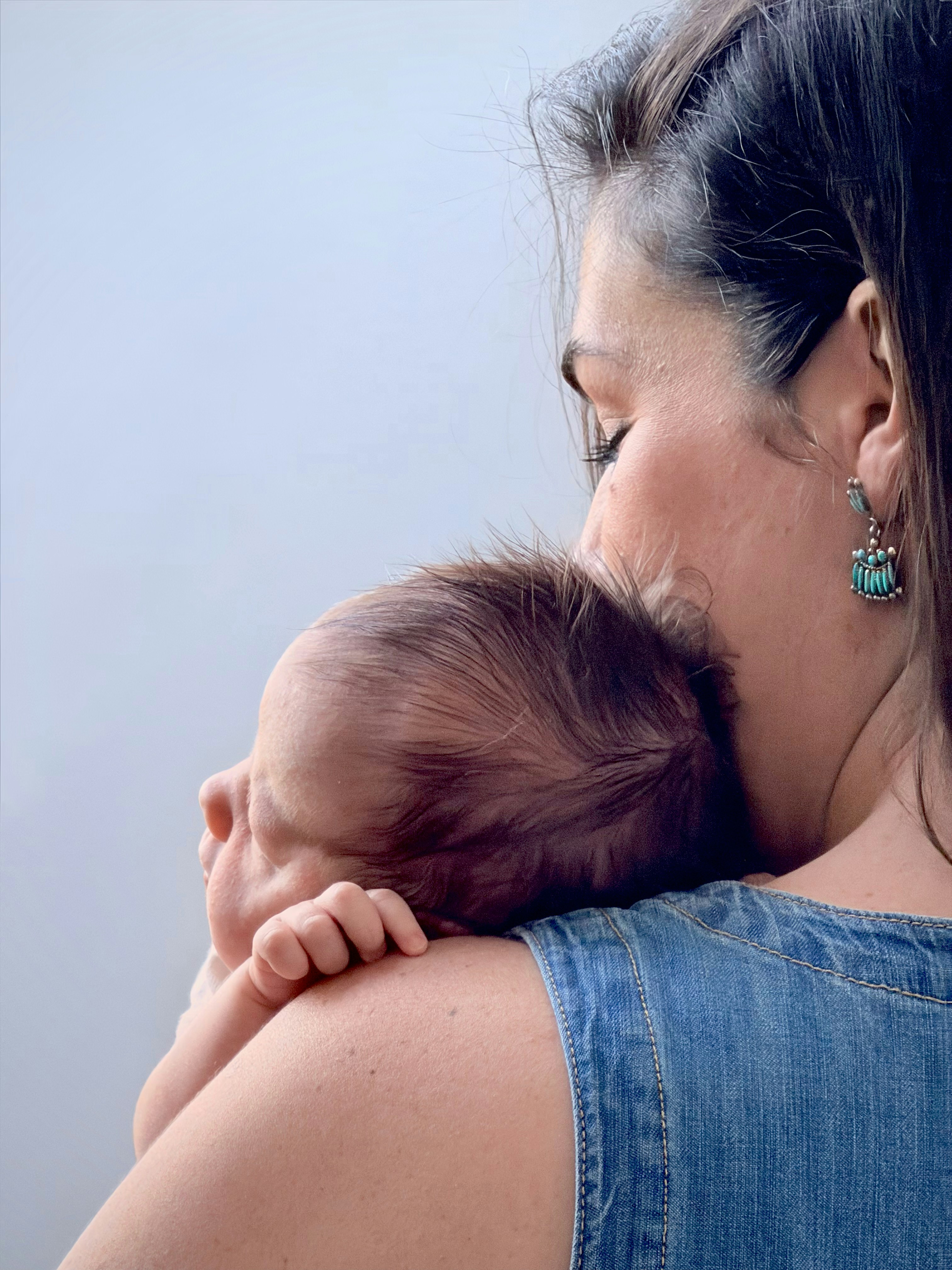 A woman in a denim top holding a baby against her shoulder