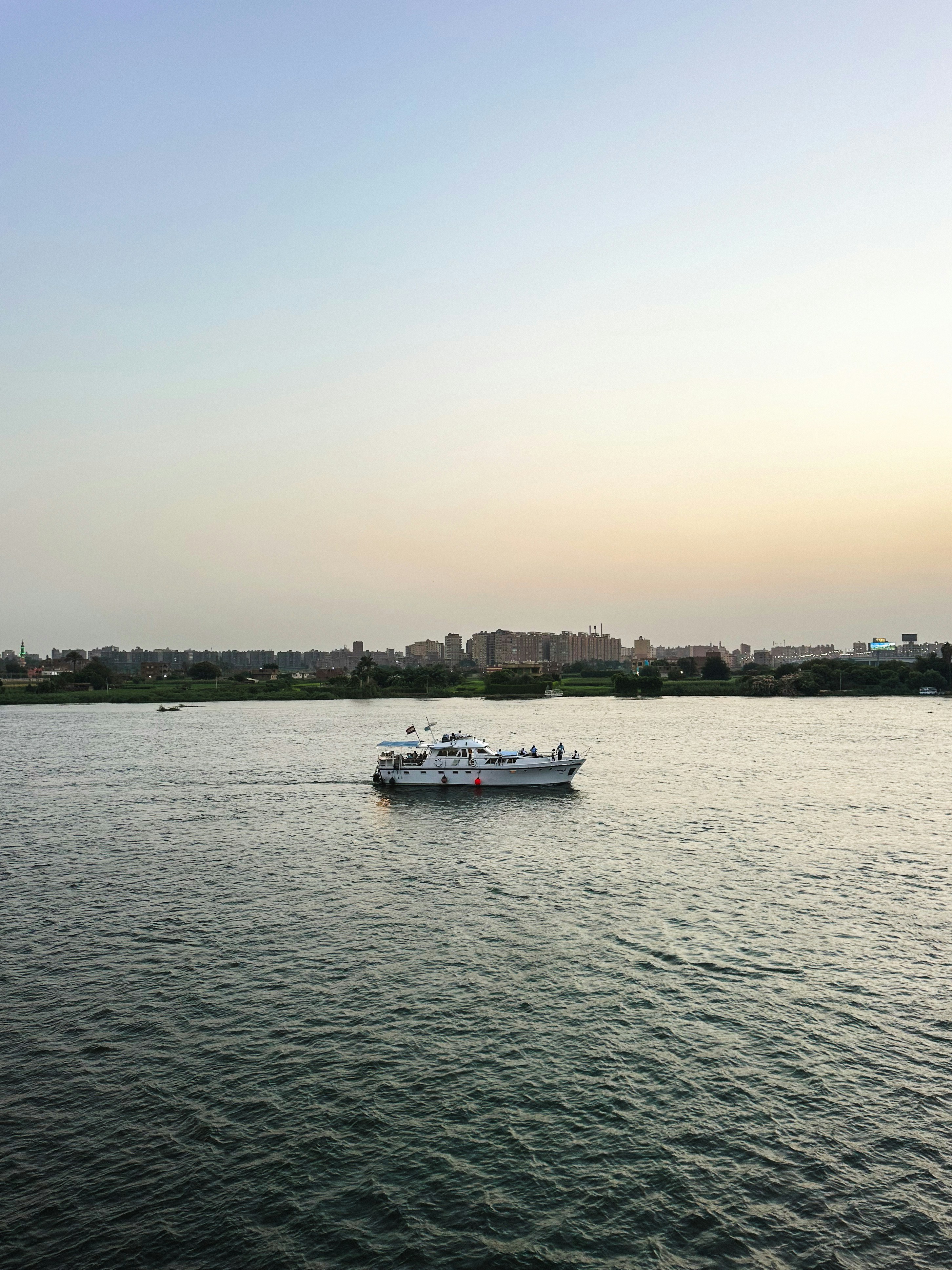 A white motorboat cruising on the Nile river with a city skyline in distance