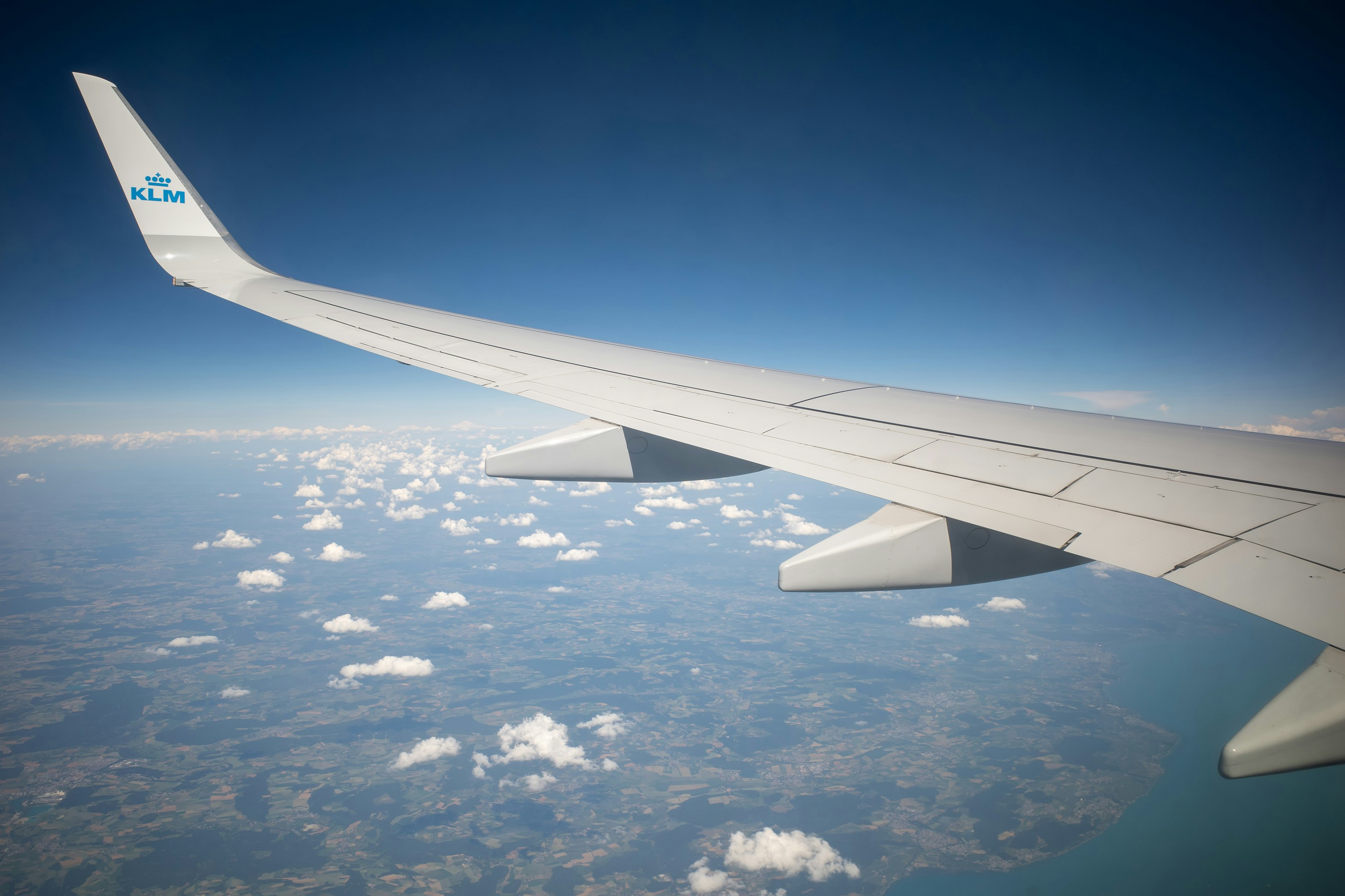 The wing of a KLM airplane above a landscape with scattered clouds, over the route used in the JFK to LAX worked example