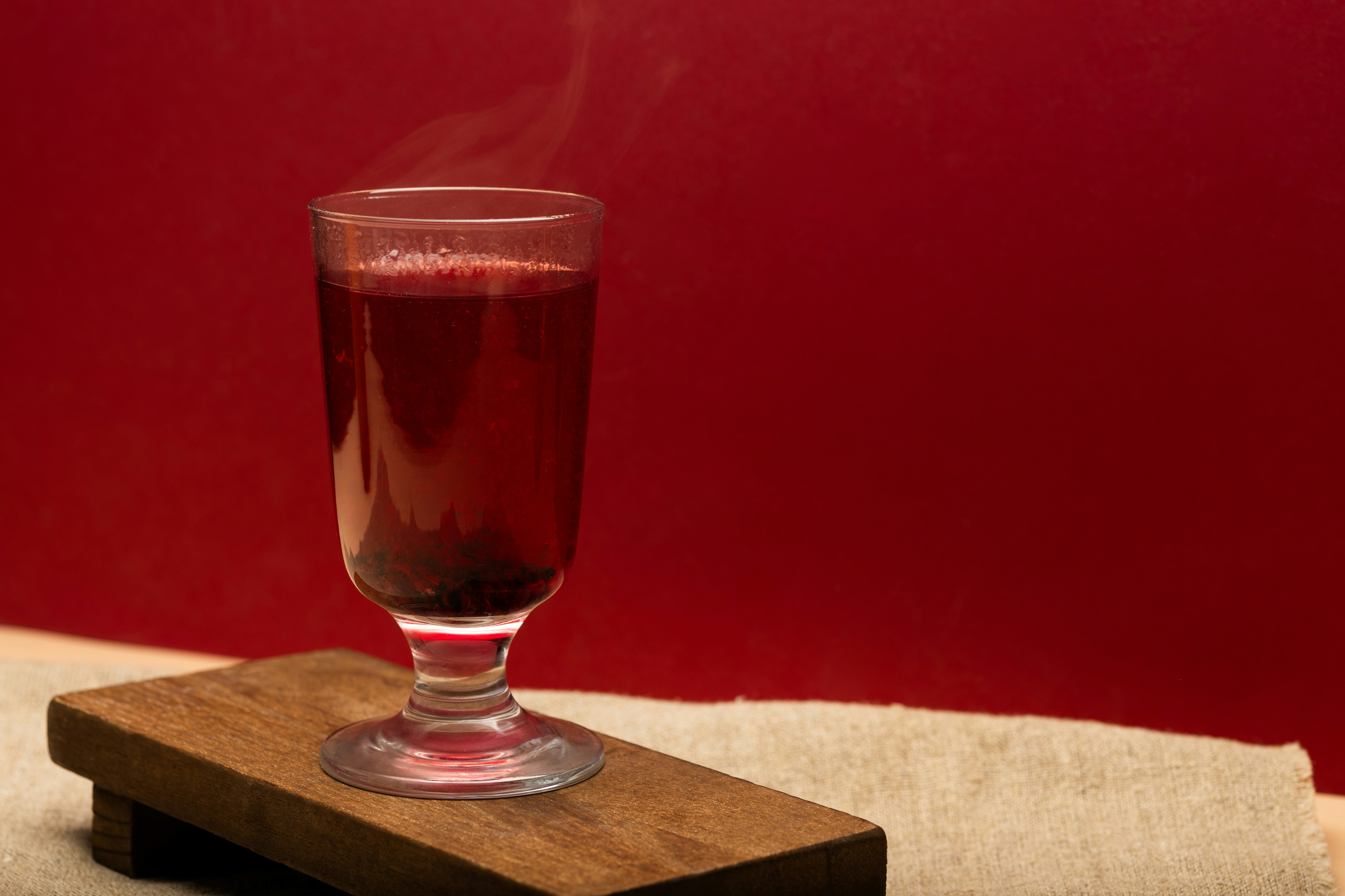 A steaming glass of red liquid on a wooden board against a red background