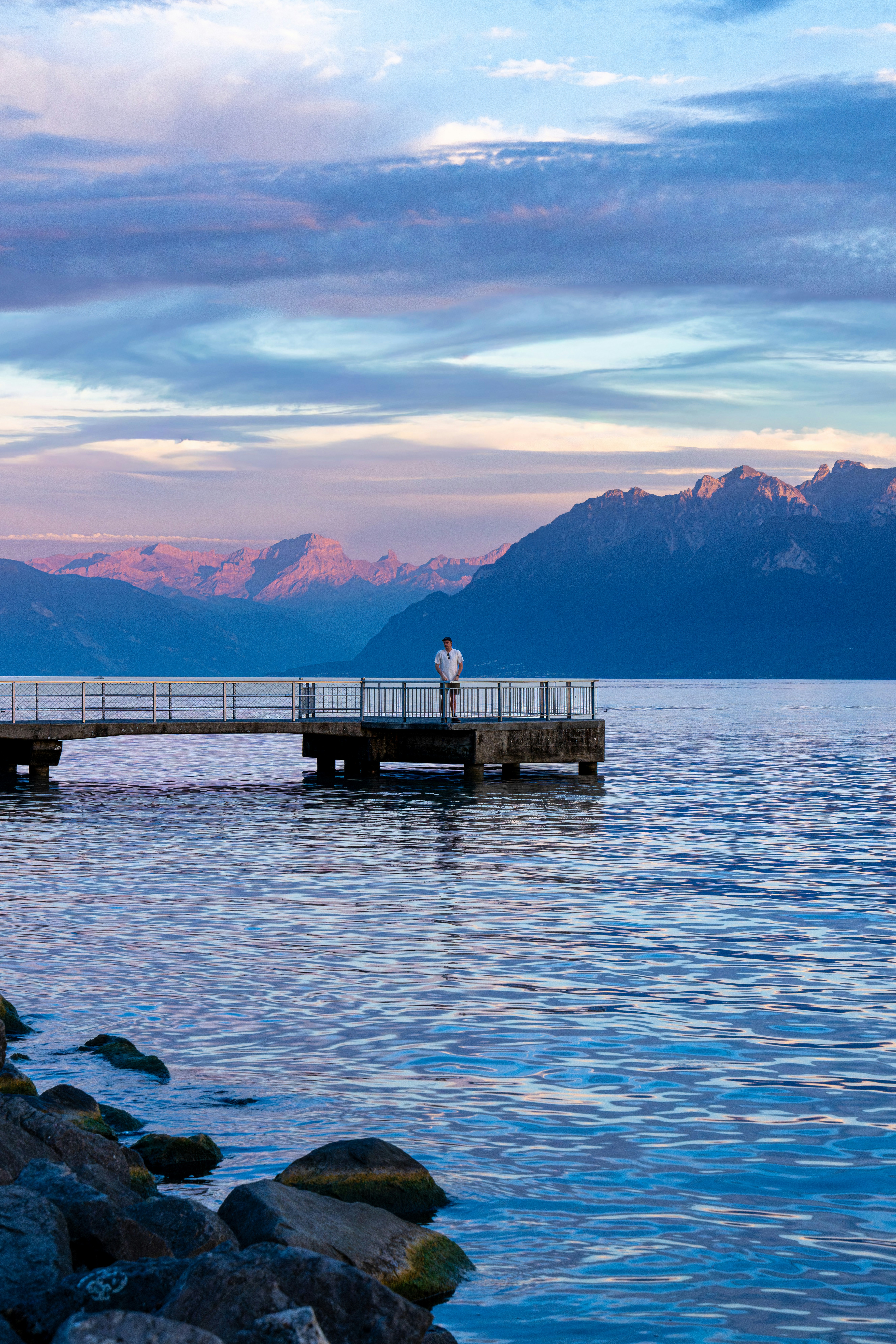 A person on a concrete pier extending into a lake with distant mountains