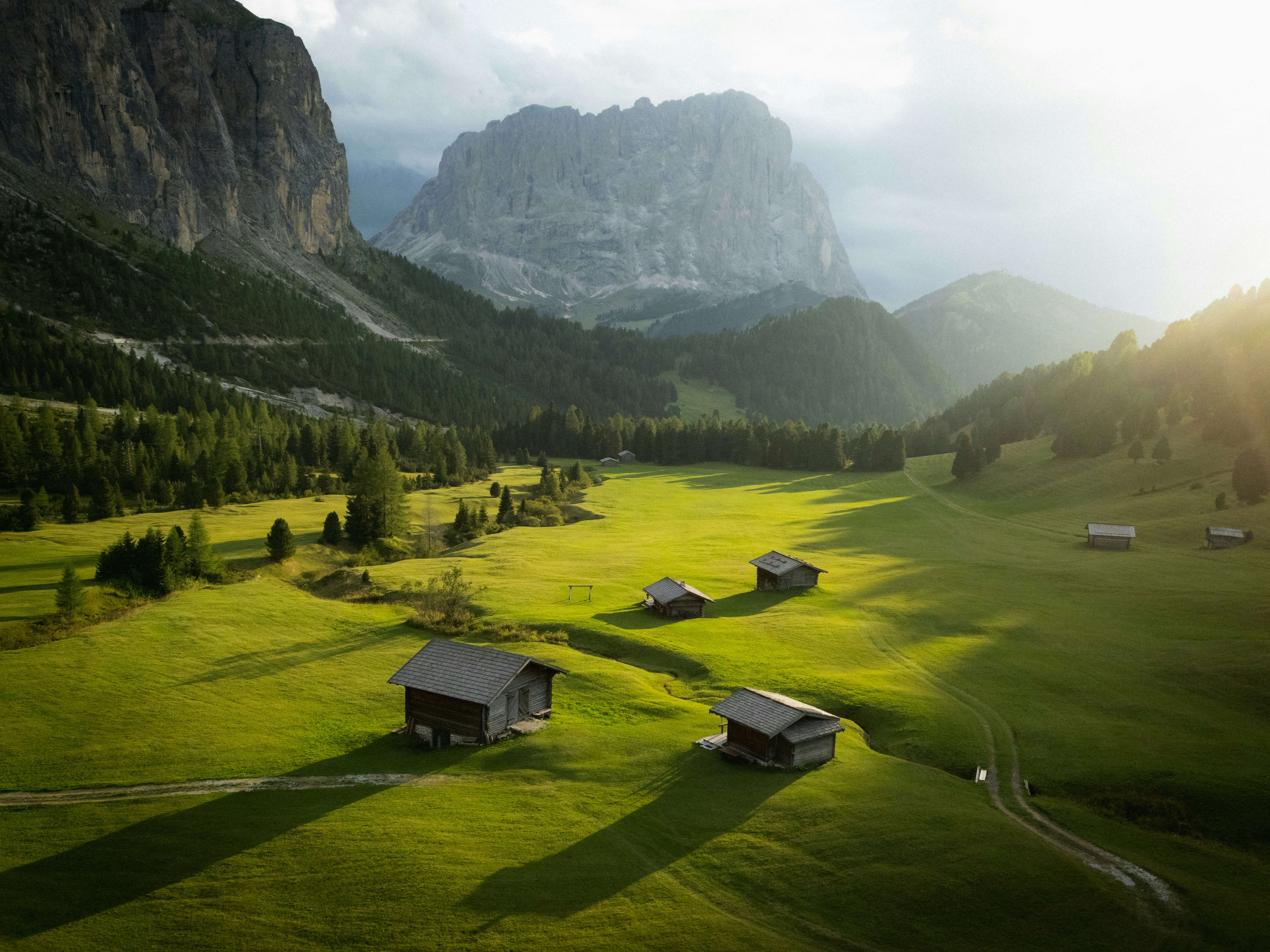 Wooden huts in a green meadow beneath the rocky peaks of the Dolomites