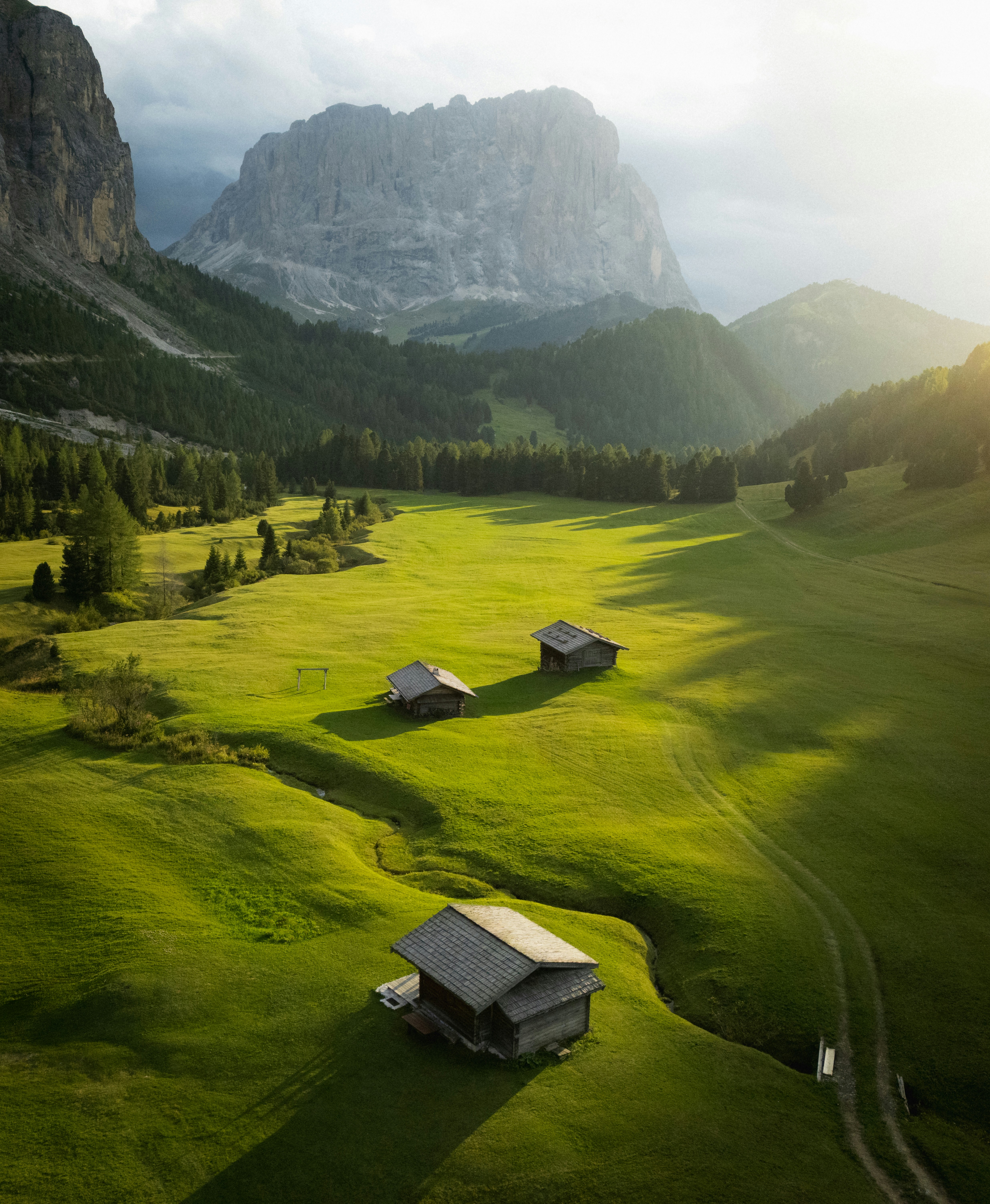 Three wooden cabins in a green meadow beneath the Dolomiti mountains
