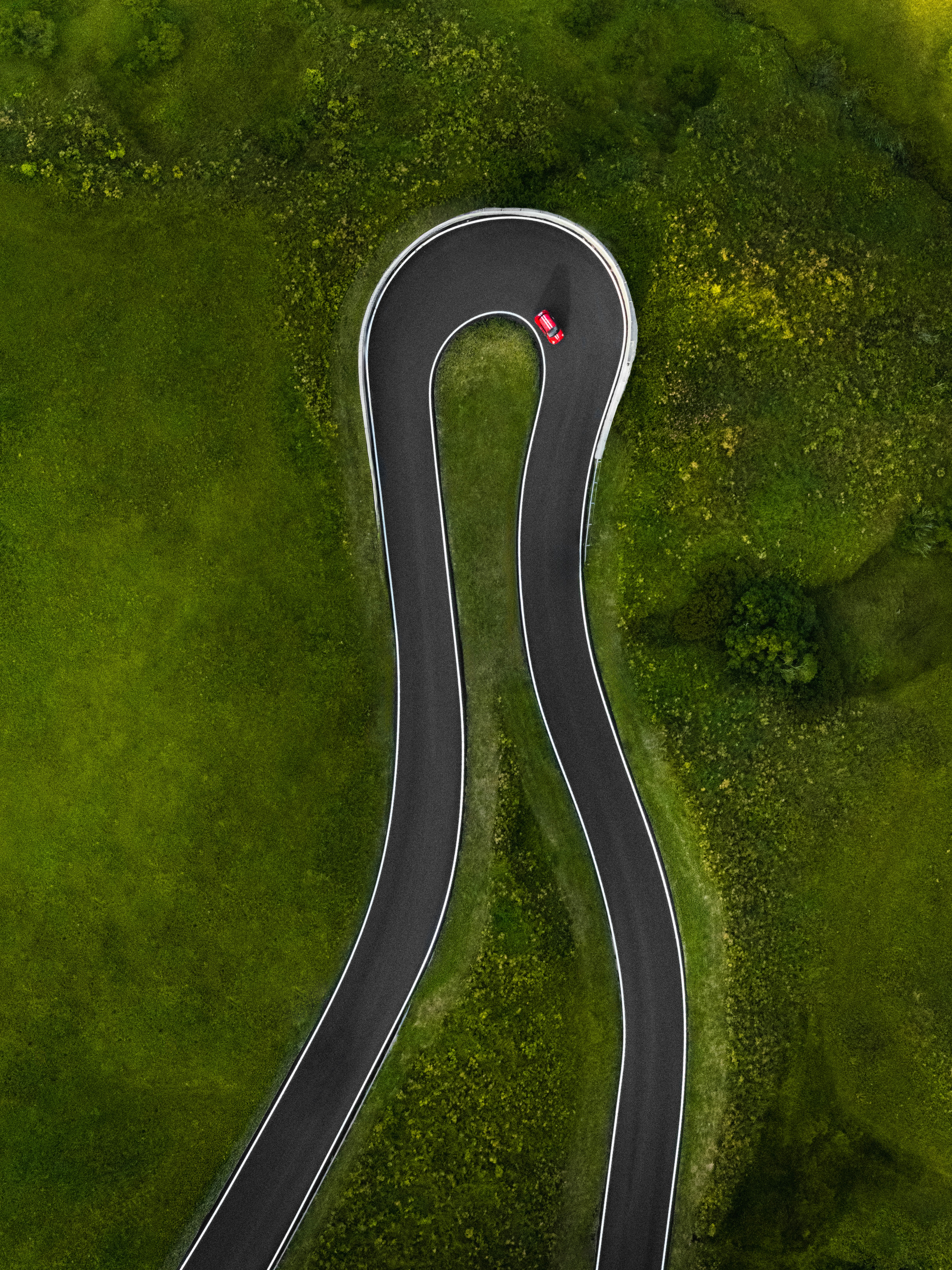 A red car driving on a winding mountain road in the Dolomites