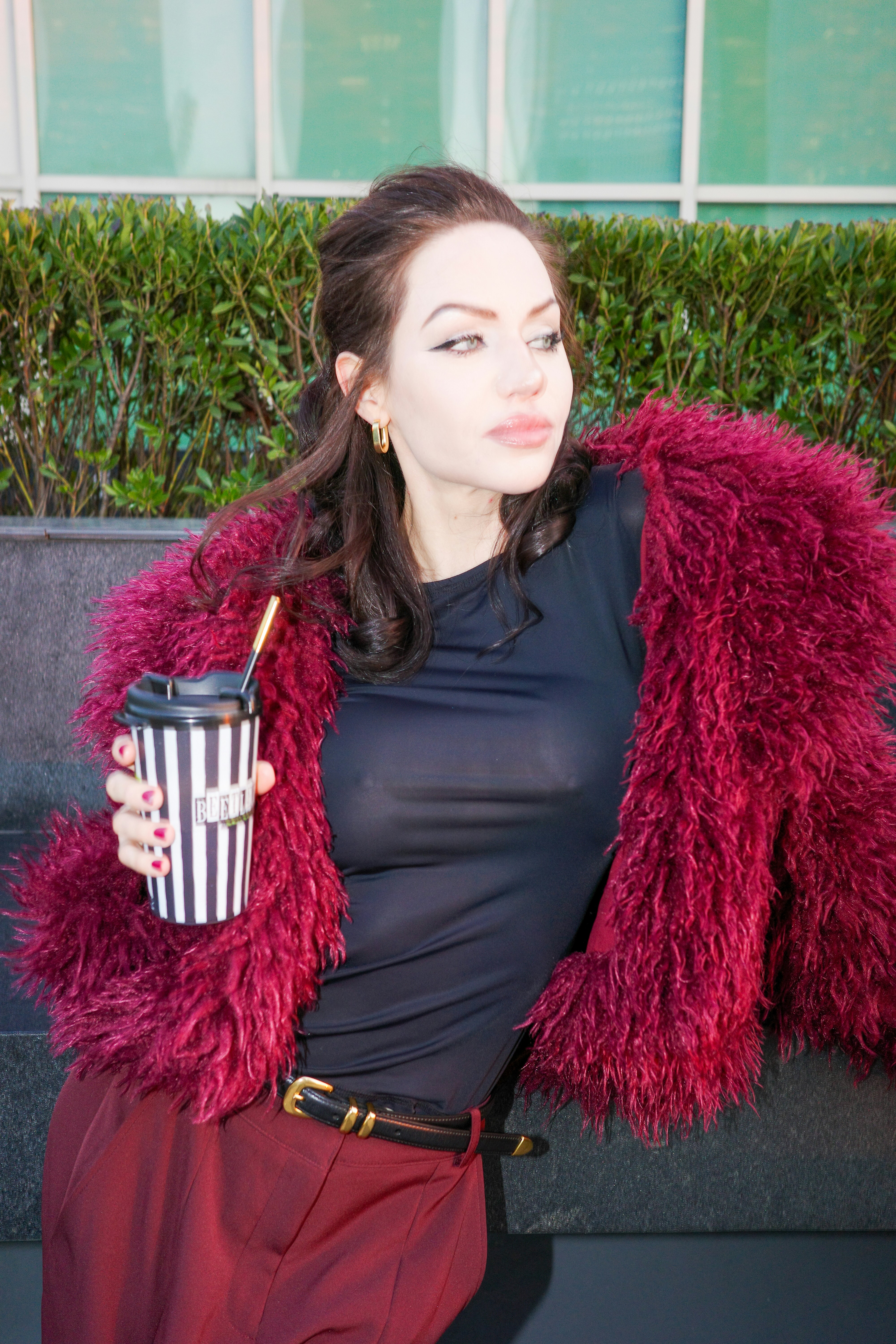 A woman in a burgundy faux fur coat holding a striped coffee cup